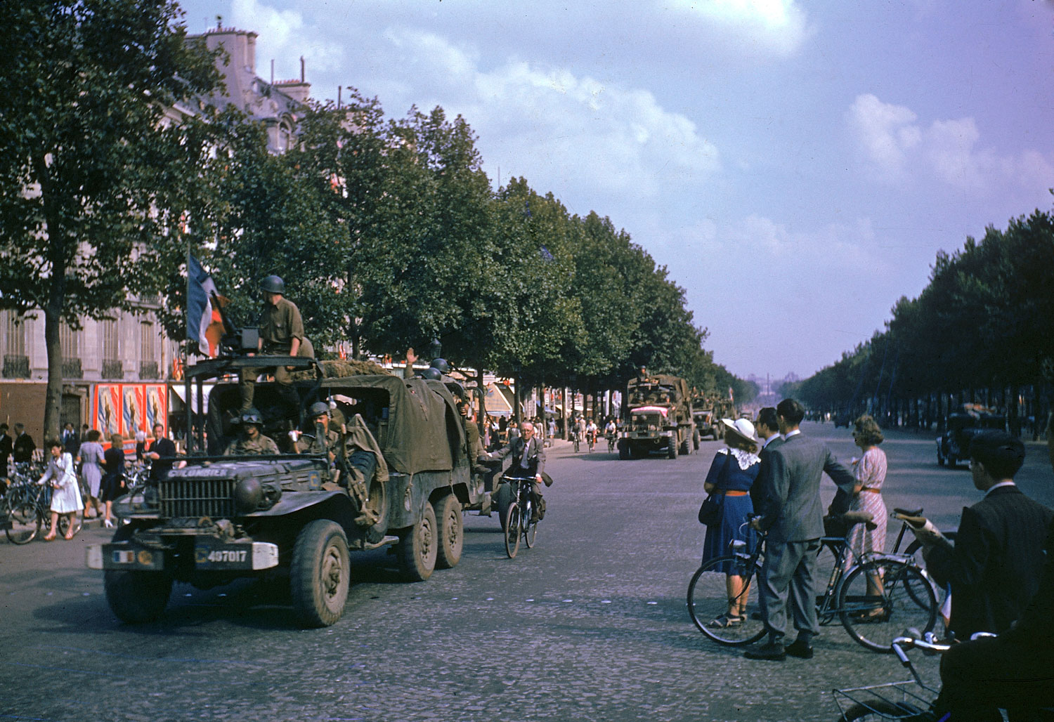 American Army trucks (note cyclist hitching a ride) parade down the Champs-Elysées the day after the liberation of Paris by French and Allied troops, August 1944.