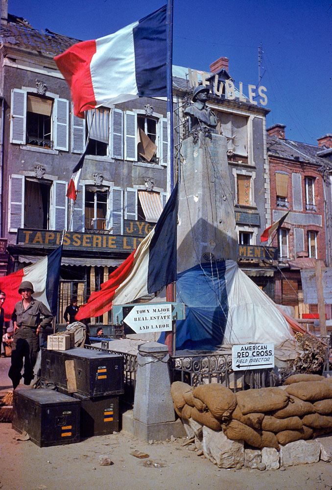 American troops stand beside a World War 1 monument bedecked with French flags after the town (exact location unknown) was liberated from German occupying forces, summer 1944.