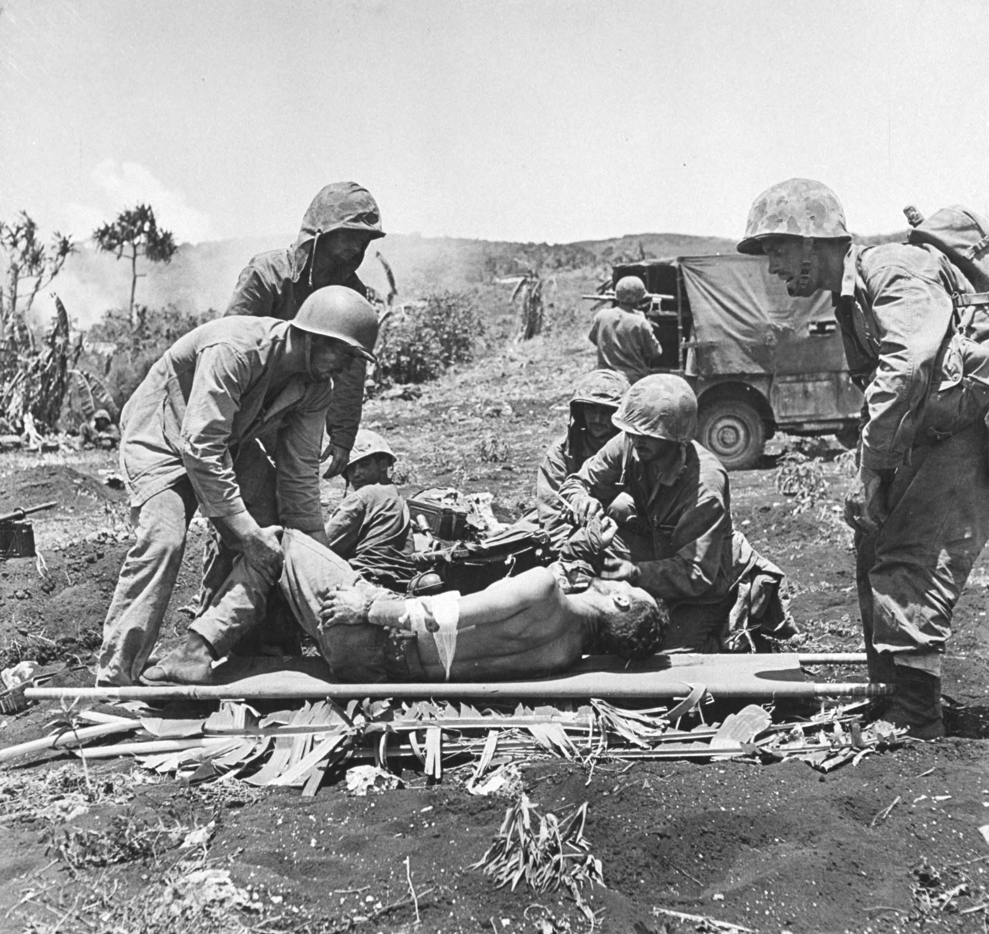 Marines tende to wounded comrades while the fighting rages on during the battle to take Saipan from the Japanese, 1944.