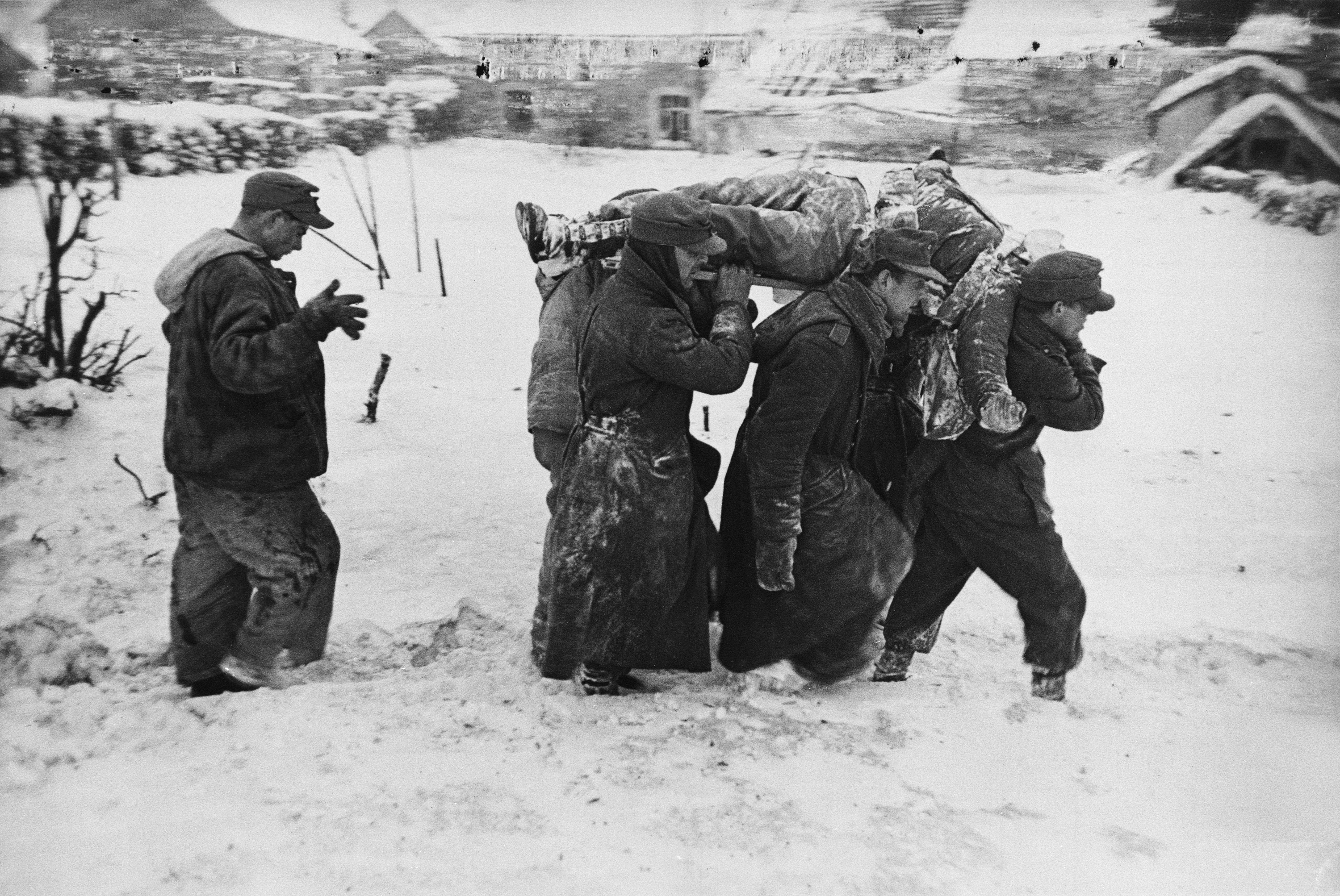 German POWs carry the body of an American soldier killed in the Battle of Bulge, January 1945.