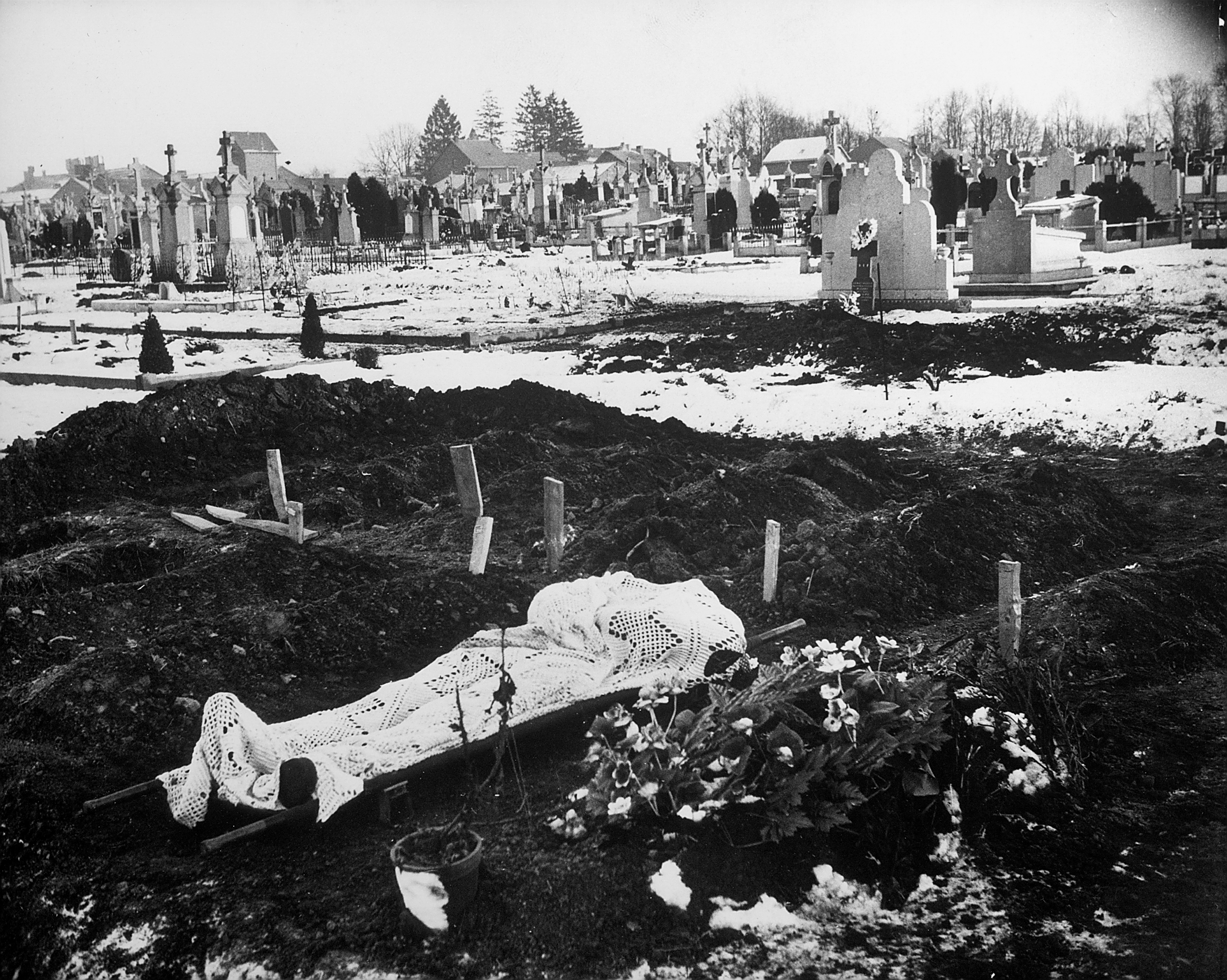 Lace curtain shrouds body of an American soldier awaiting burial in Bastogne cemetery, January 1945.