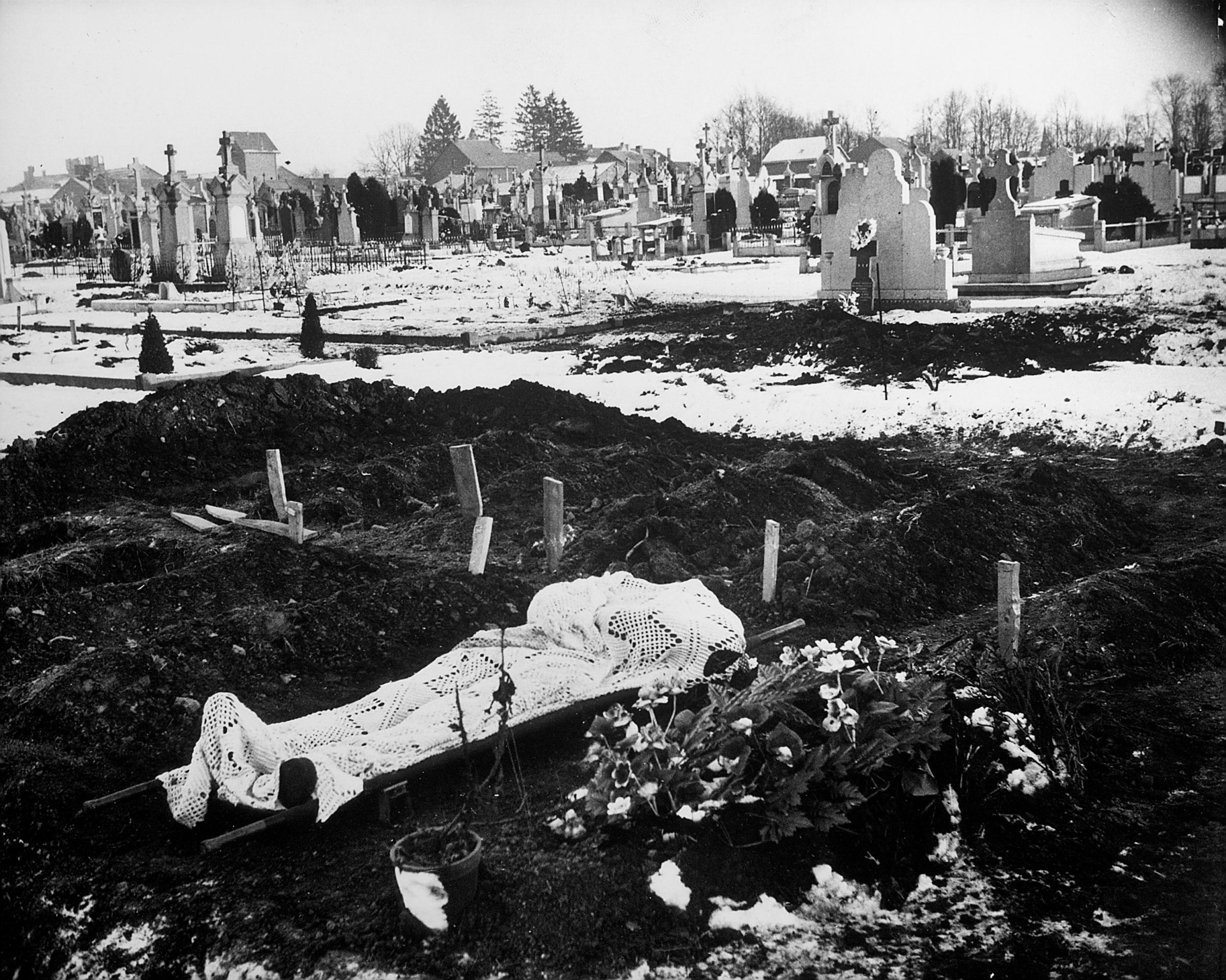 Lace curtain shrouds body of an American soldier awaiting burial in Bastogne cemetery, January 1945.
