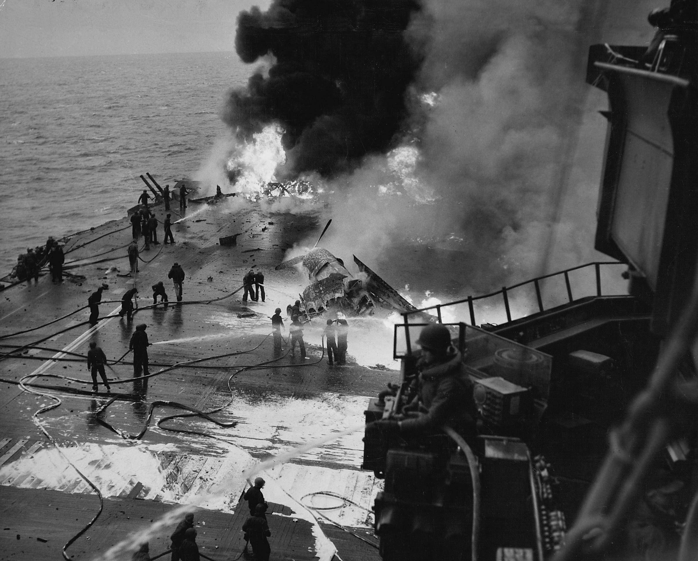 Crewmen fight fires on the deck of the USS Saratoga, which was badly damaged and set ablaze after being hit several times by Japanese bomber planes and kamikaze attacks off of Iwo Jima, 1945.