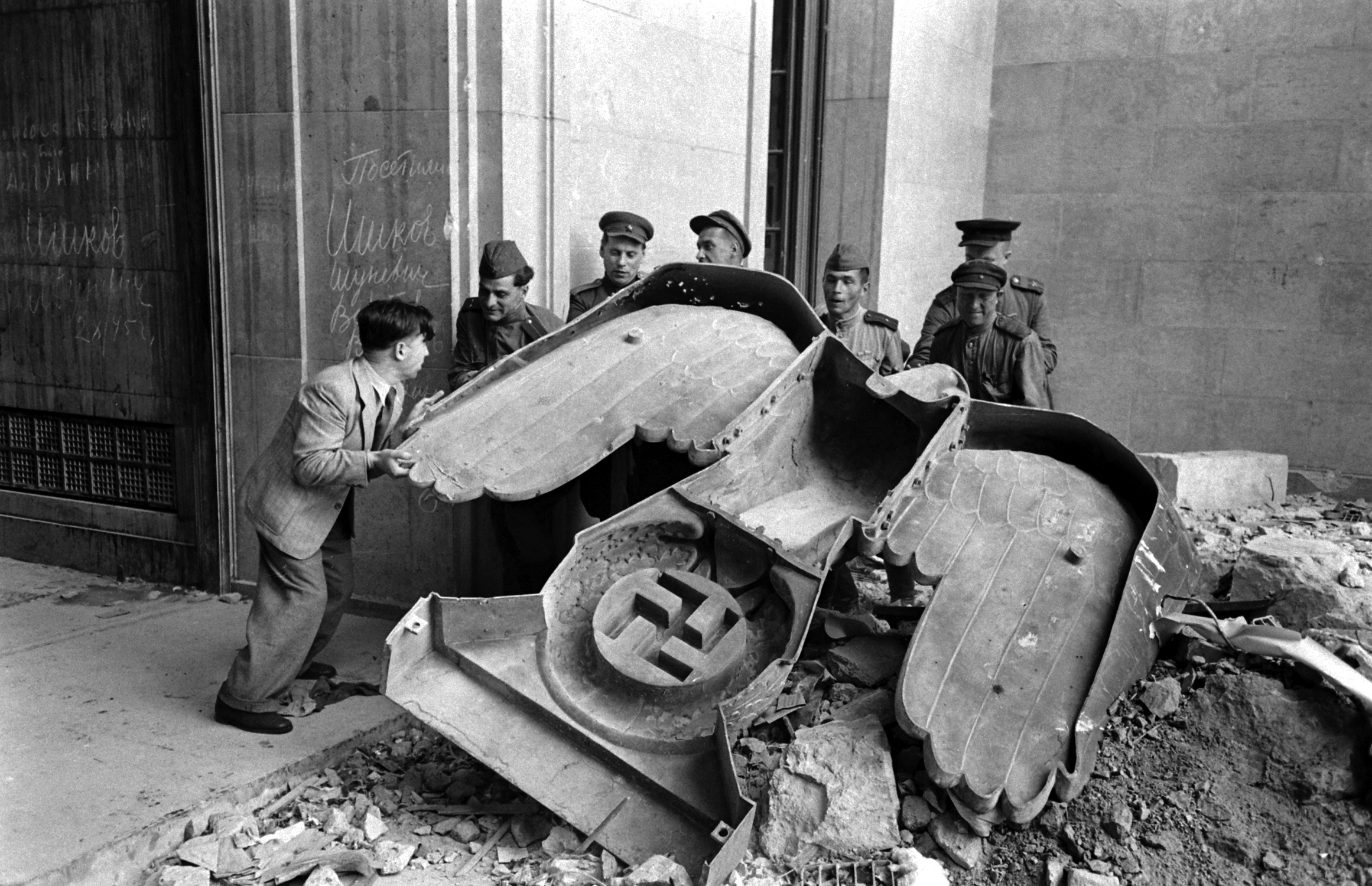 Russian soldiers and a civilian struggle to move a large bronze Nazi Party eagle that once loomed over a doorway of the Reich Chancellery, Berlin, 1945.