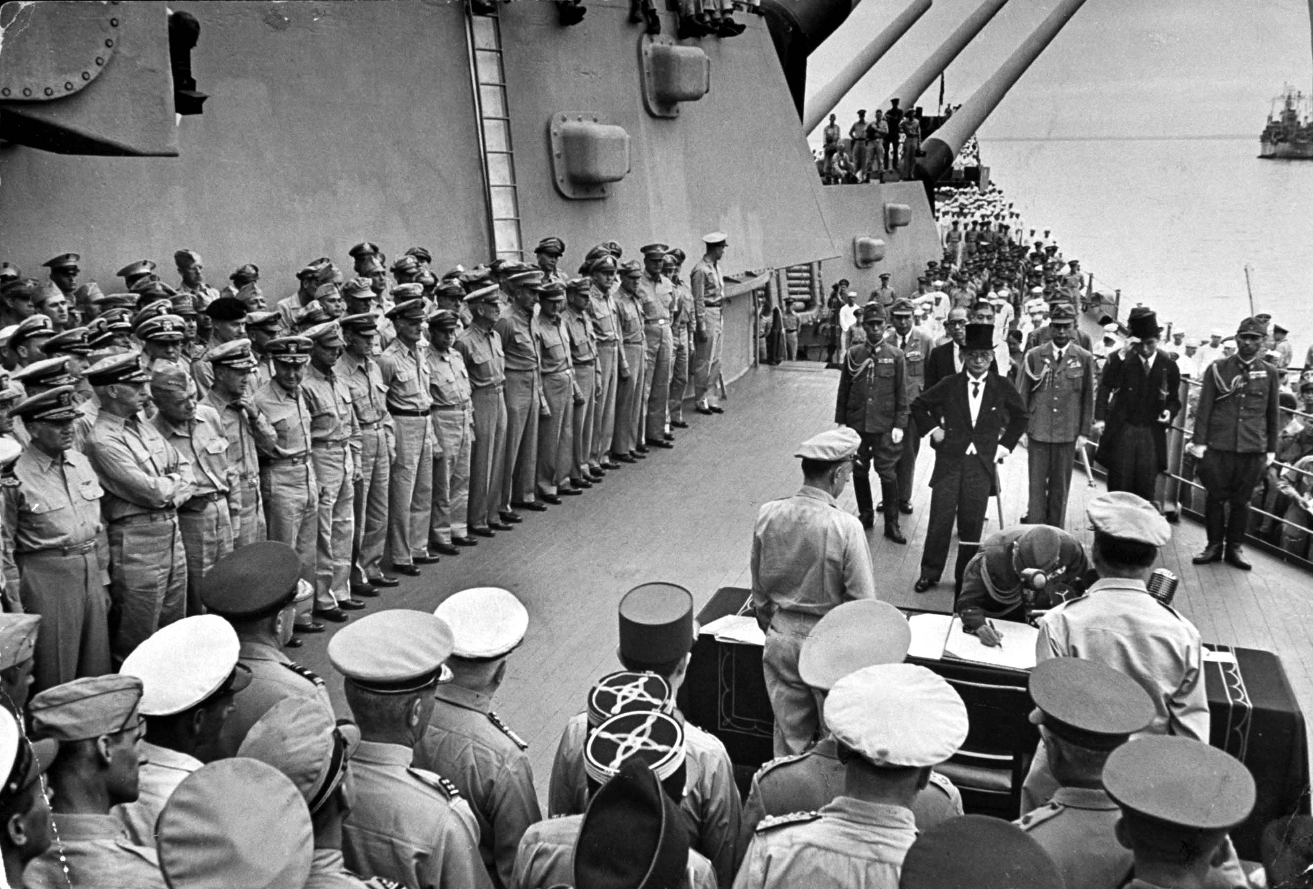 American officers (including neck-craning skeptic William  Bull  Halsey, third fr. left) line deck of battleship USS Missouri (BB-63) while Japanese delegation signs official surrender document, Sept. 2, 1945.