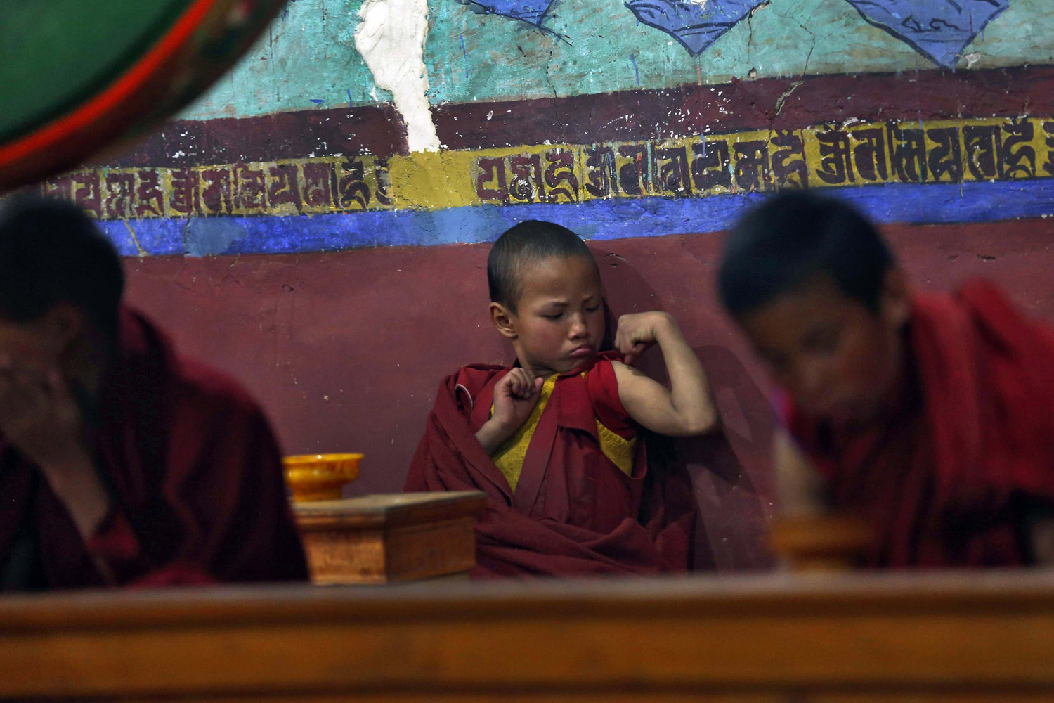 A young Buddhist monk flexes his muscles during morning prayers at Thikse Monastery