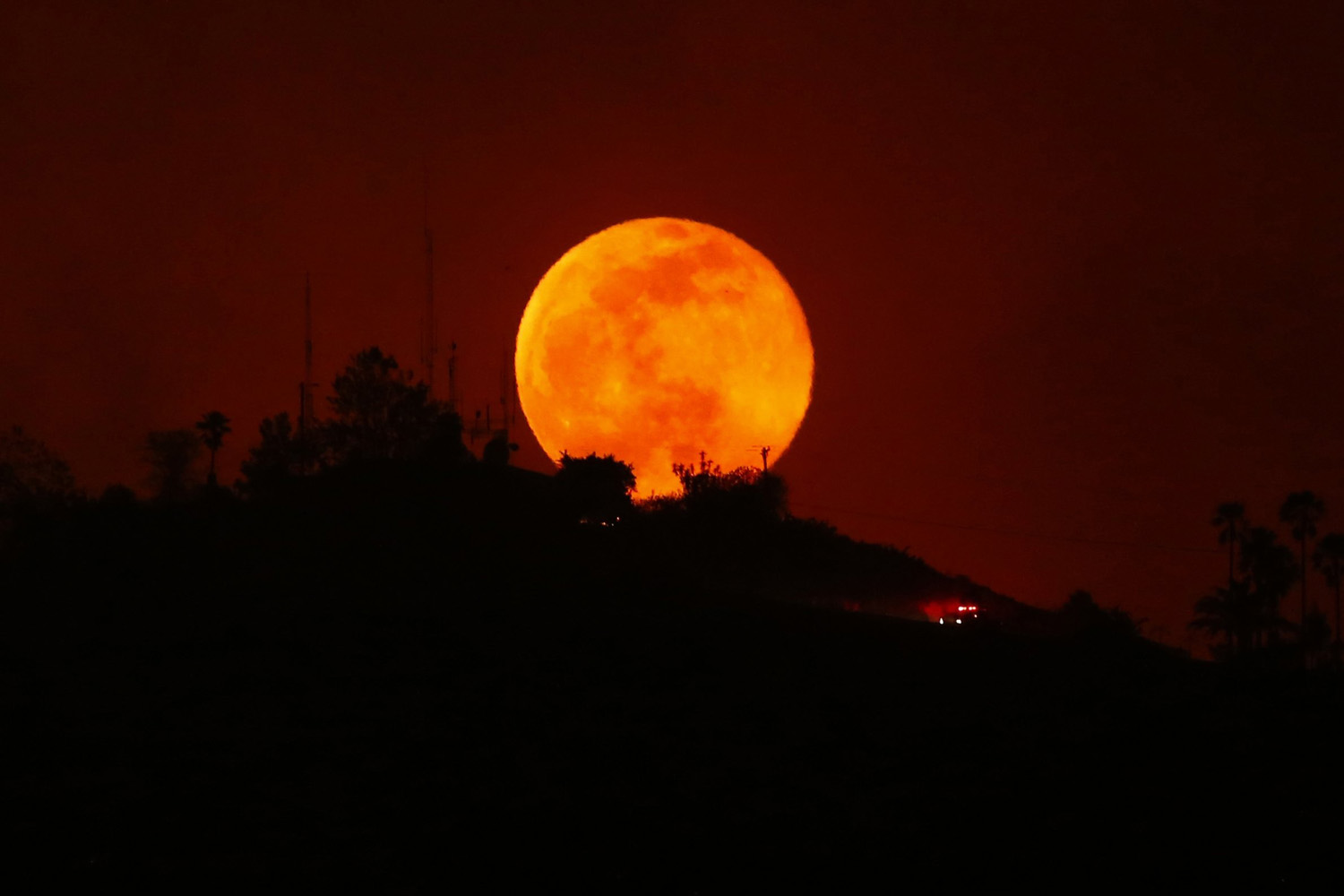 An emergency vehicle makes is way past a rising moon as it travels along a burned-out hillside near San Marcos