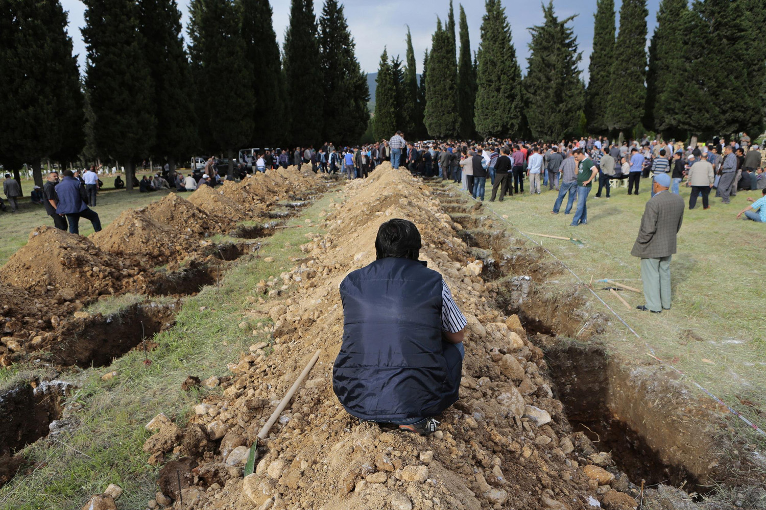 A man sits near graves during the funeral of a miner who died in a fire at a coal mine, in Soma