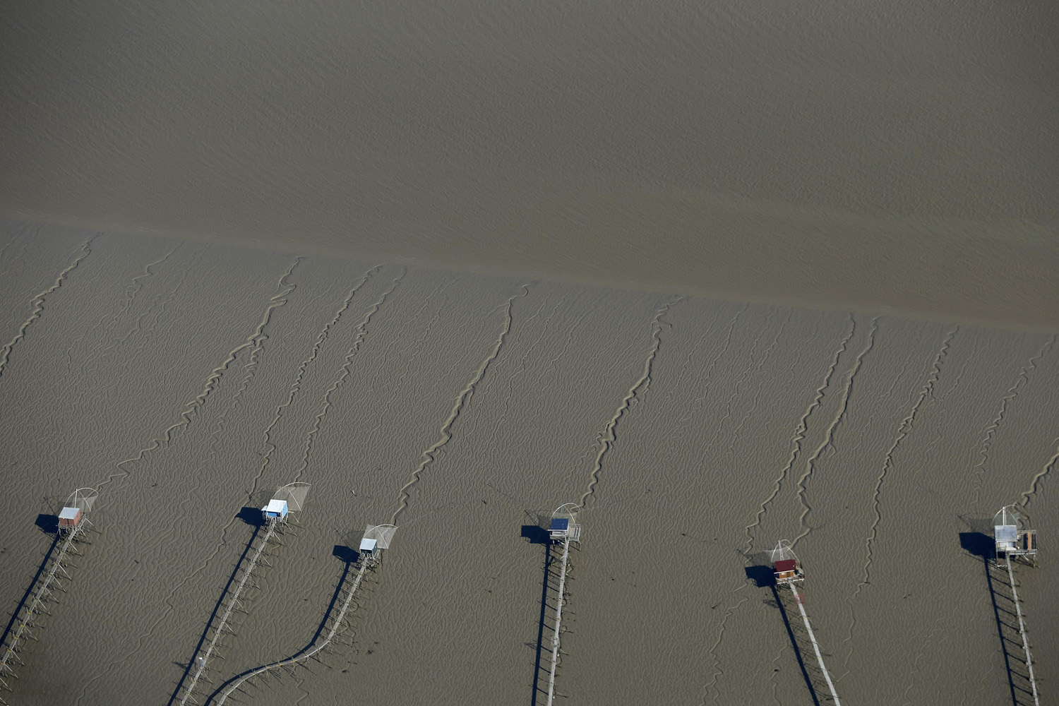 Lines mark the sand during low tide in the Loire Estuary in this aerial view with cabins and their tradition hanging fish nets in Paimboeuf