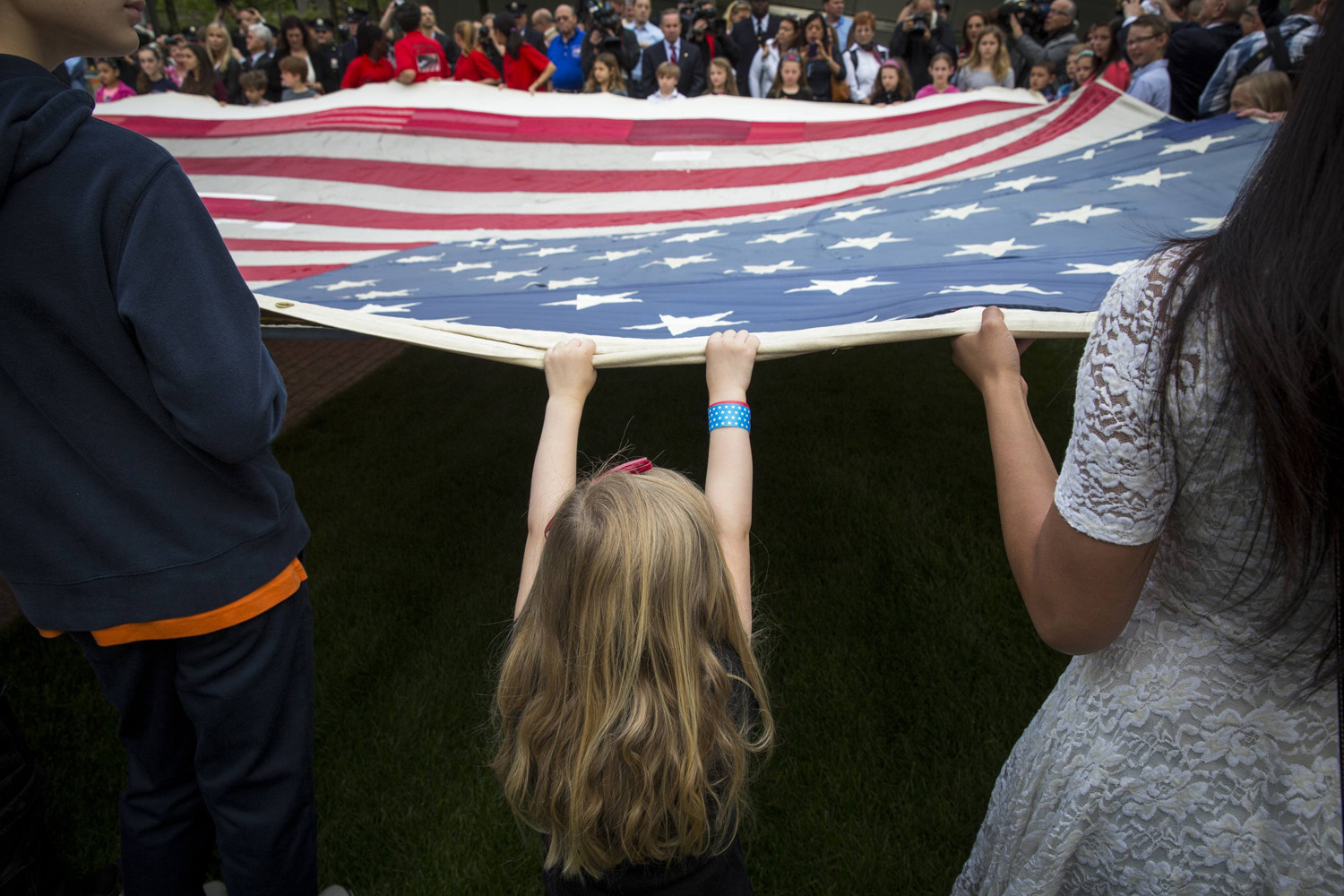 A girl designated to assist with transferring the National 9/11 Flag holds it aloft on the grounds of the 9/11 Memorial Plaza before donating it to the National September 11 Memorial Museum in New York