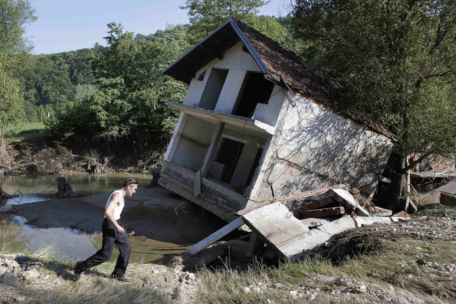 A man walks past a house tilted by floods in the town of Valjevo, southwest from Belgrade