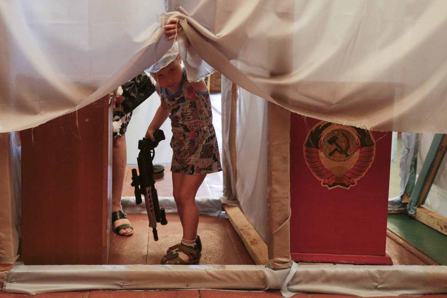 A child looks out as voters fill out ballot papers in booths during voting in a presidential election at a polling station in the village of Kodra