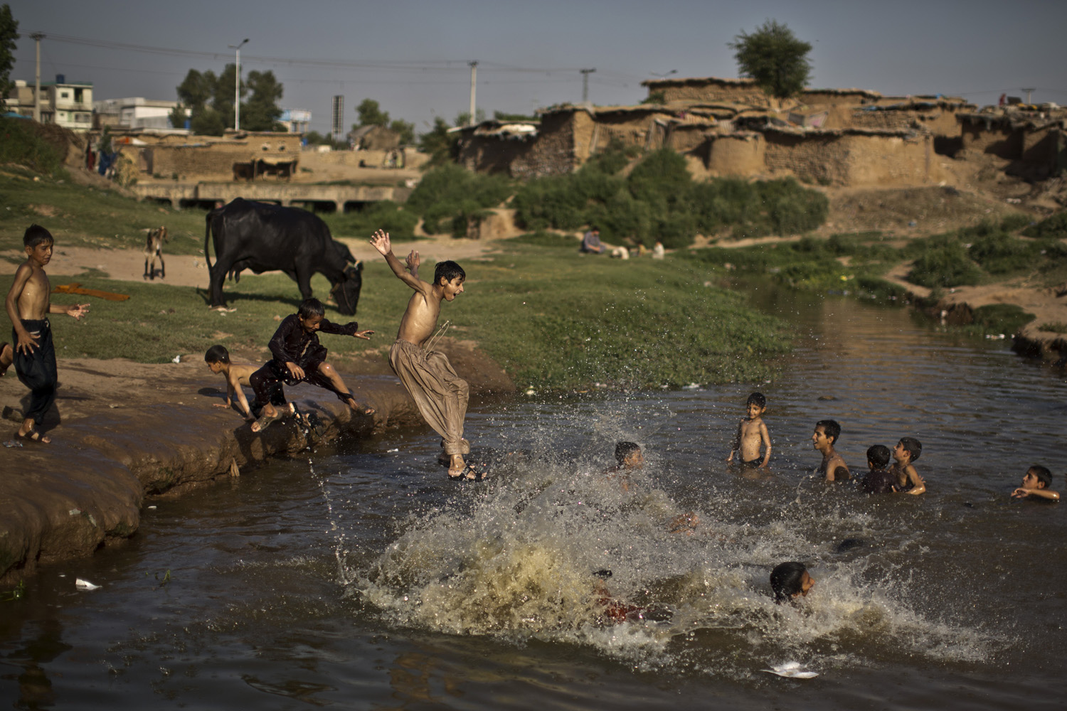 An Afghan refugee boy jumps into the water while he and others swim in a polluted stream to cool off as the temperature rises, on the outskirts of Islamabad, Pakistan on May 28, 2014.