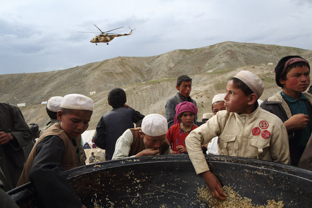 Children eat from one of several giant cooking pans as an Afghan National Army helicopter departs the site, May 5, 2014.