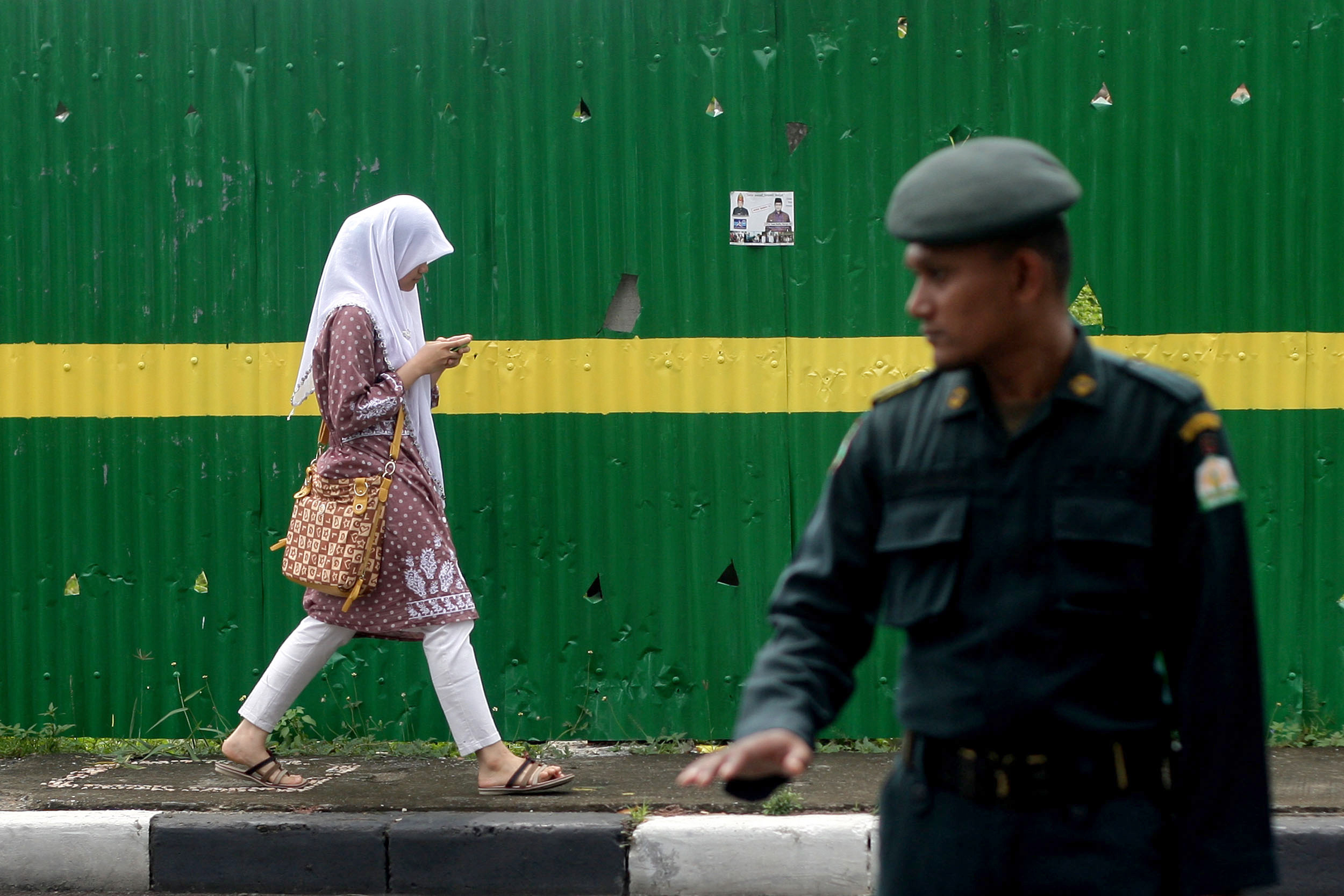 An Acehnese Shari‘a police officer mans a checkpoint as a Muslim woman walks past in Banda Aceh, Aceh province, Indonesia, in October 2013 (Heri Juanda—AP)