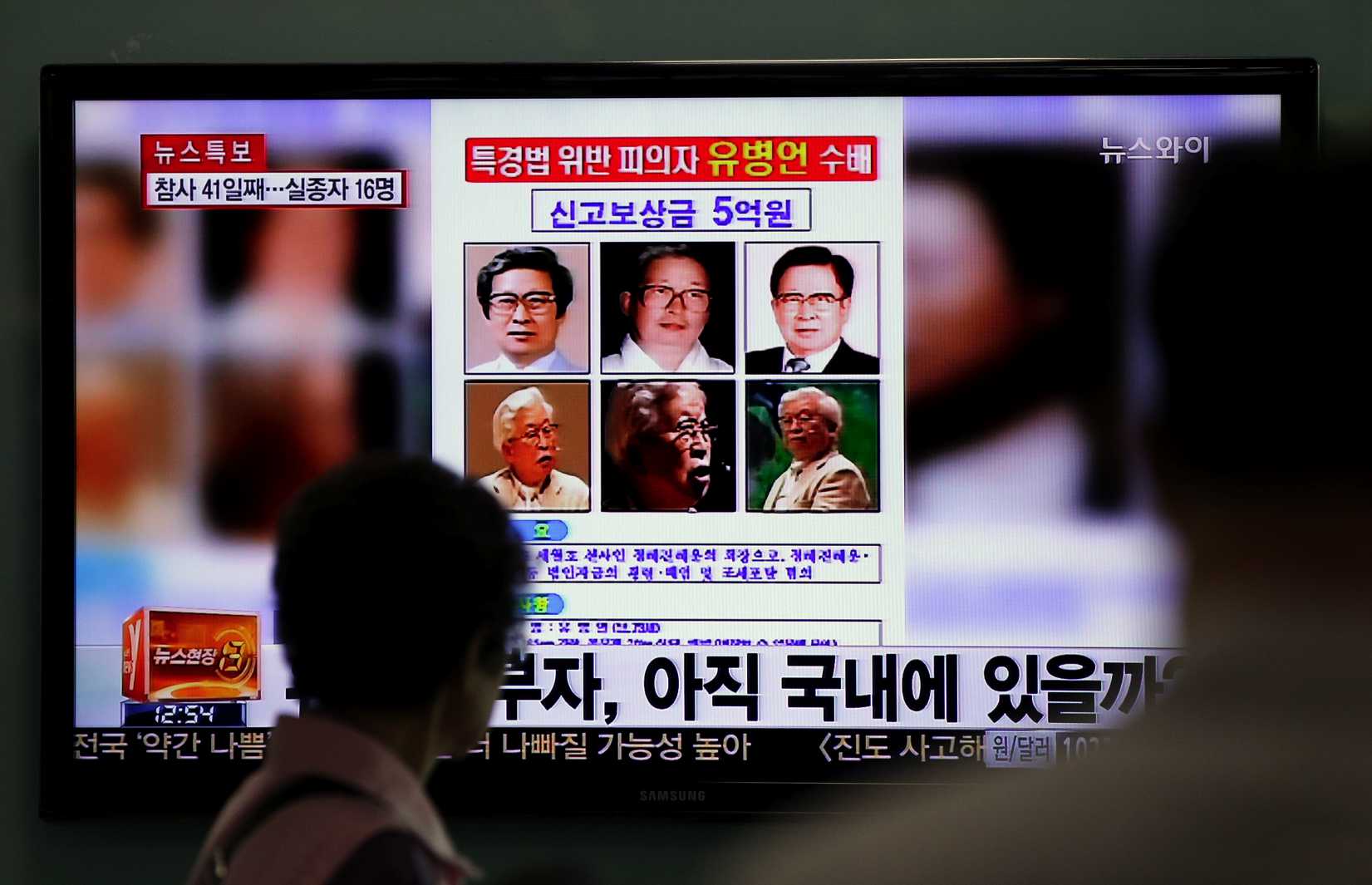 Commuters at a train station in Seoul walk past a screen displaying the wanted poster for Yoo Byung-eun and others, on Monday, May 26, 2014. (Lee Jin-man—AP)