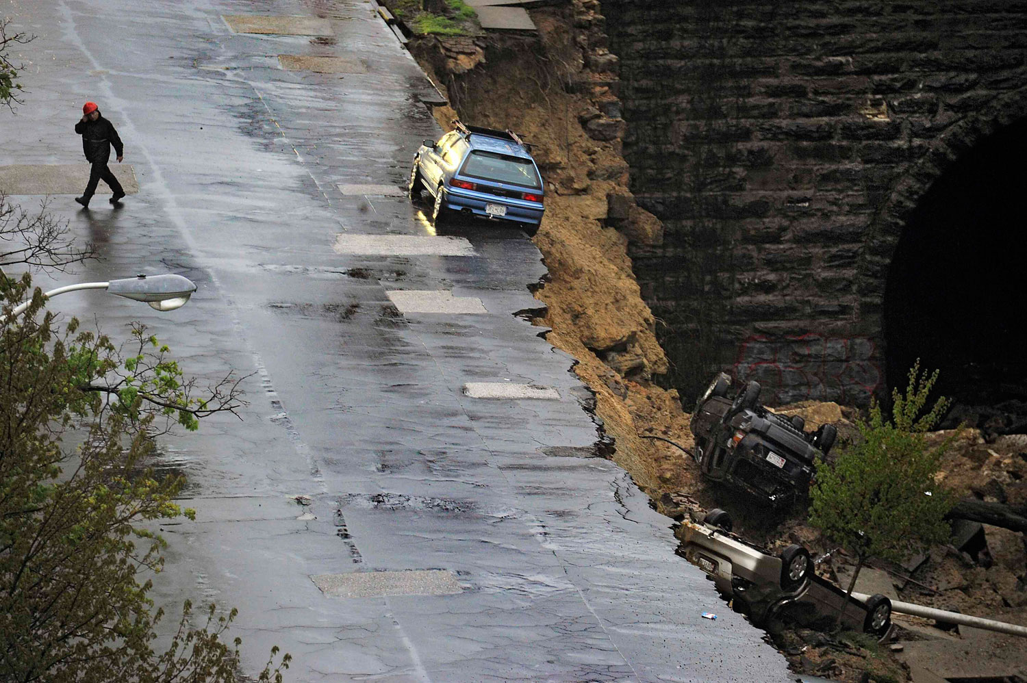 An emergency worker walks on the other side of the street where one car still rests precariously after a retaining wall collapsed beneath a row of vehicles in Baltimore, Maryland, April 30, 2014.