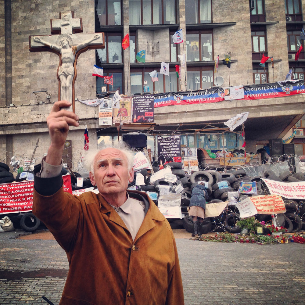 May 8, 2014. A man holds a cross up in front of the headquarters of the Donetsk People's Republic in Donetsk, Ukraine.