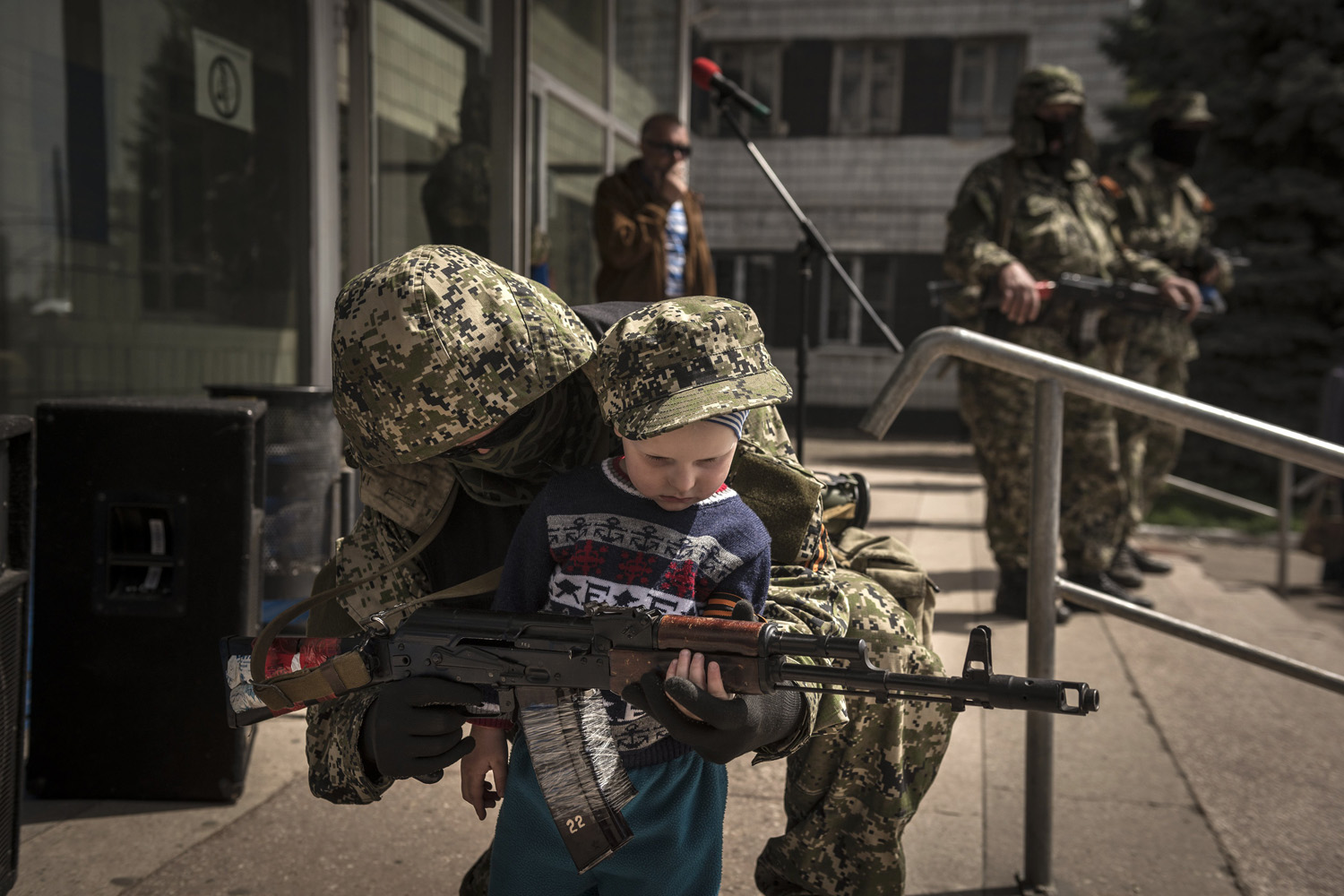 A pro-Russia militia member standing guard outside a seized government building allows a child to partially hold his gun.