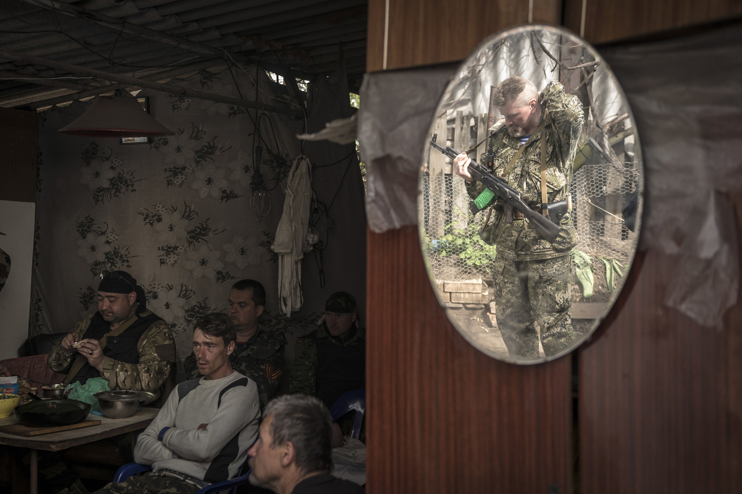 A pro-Russian militant is reflected in a mirror as he adjusts his rifle, while others watch a Victory Day military parade in Moscow on the television, as they start their day in Slovyansk, eastern Ukraine.