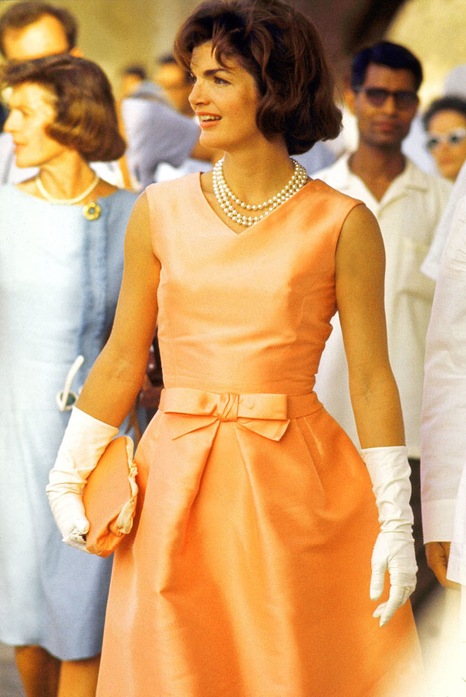 U.S. First Lady Jackie Kennedy wears a fitted silk apricot dress and triple strand of pearls, walking through crowds at Udaipur during visit to India on March 1, 1962.