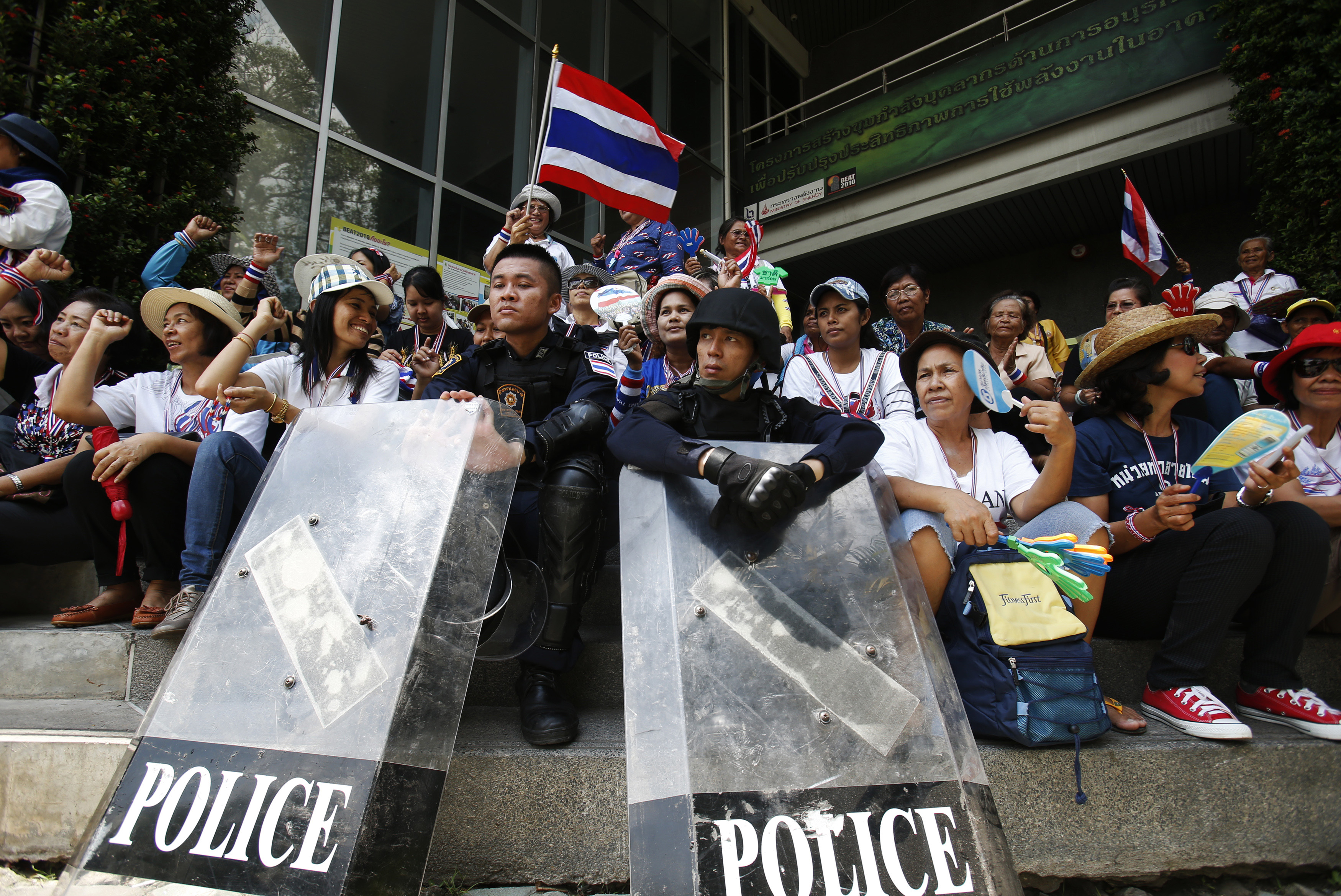 Anti-government protesters sit with riot policemen outside the NBT TV station in Bangkok