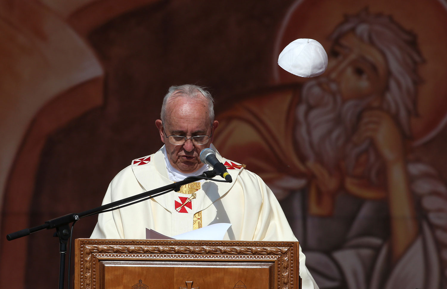 A gust of wind blows off Pope Francis' cap as he speaks during a mass at Amman International Stadium