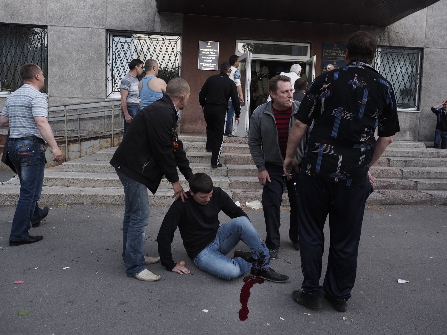 May 11, 2014. A man sits on the ground just moments after being shot in the leg by armed guards.