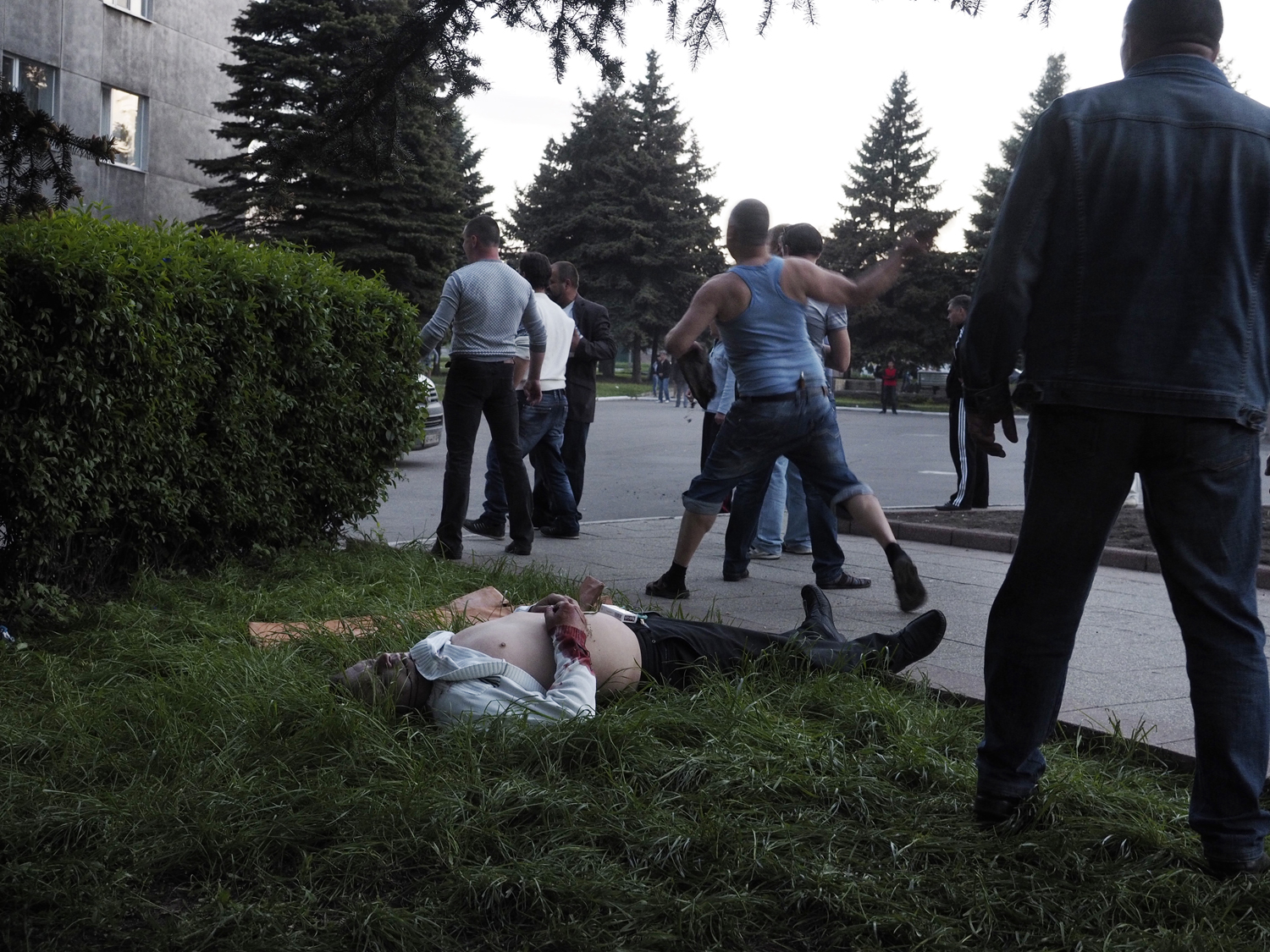 May 11, 2014. A man in blue throws an unknown object in the direction of the armed guards as the other man lies dead. Moments earlier, he had crossed the dead man's arms over his chest.