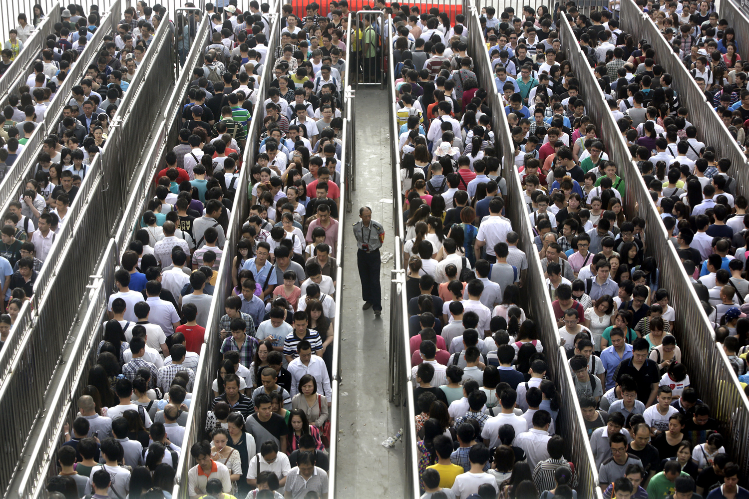 A security officer stands guard as passengers line up and wait for a security check during morning rush hour at Tiantongyuan North Station in Beijing May 27, 2014. 