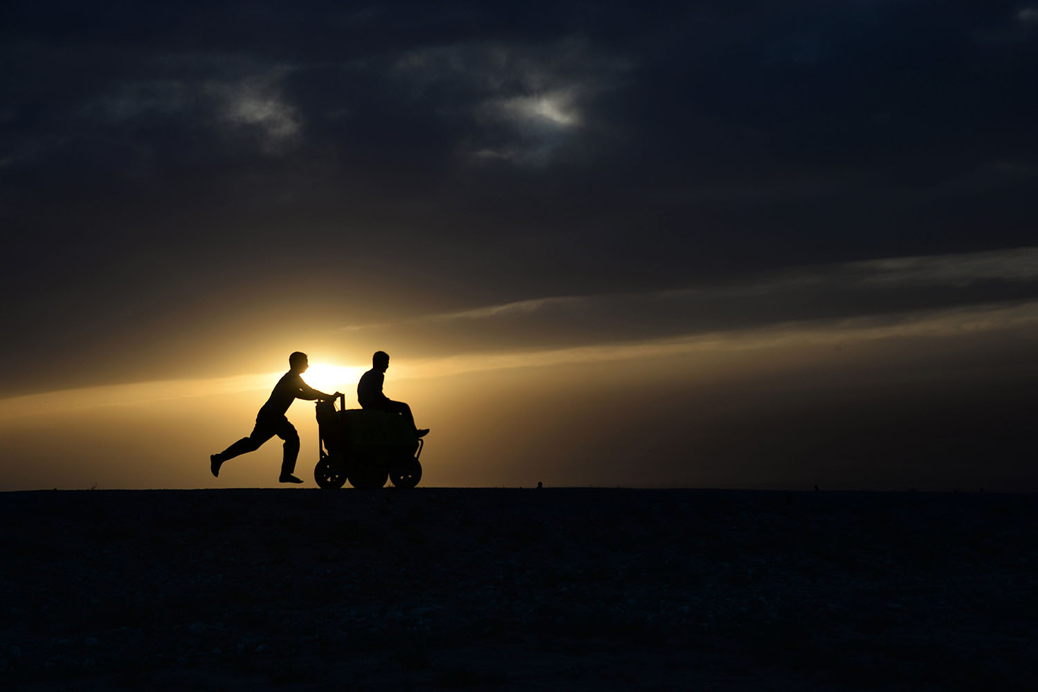 An Afghan youth pushes a friend on a ice-cream cart as the sun sets on the outskirts of Mazar Sharif on May 16, 2014.