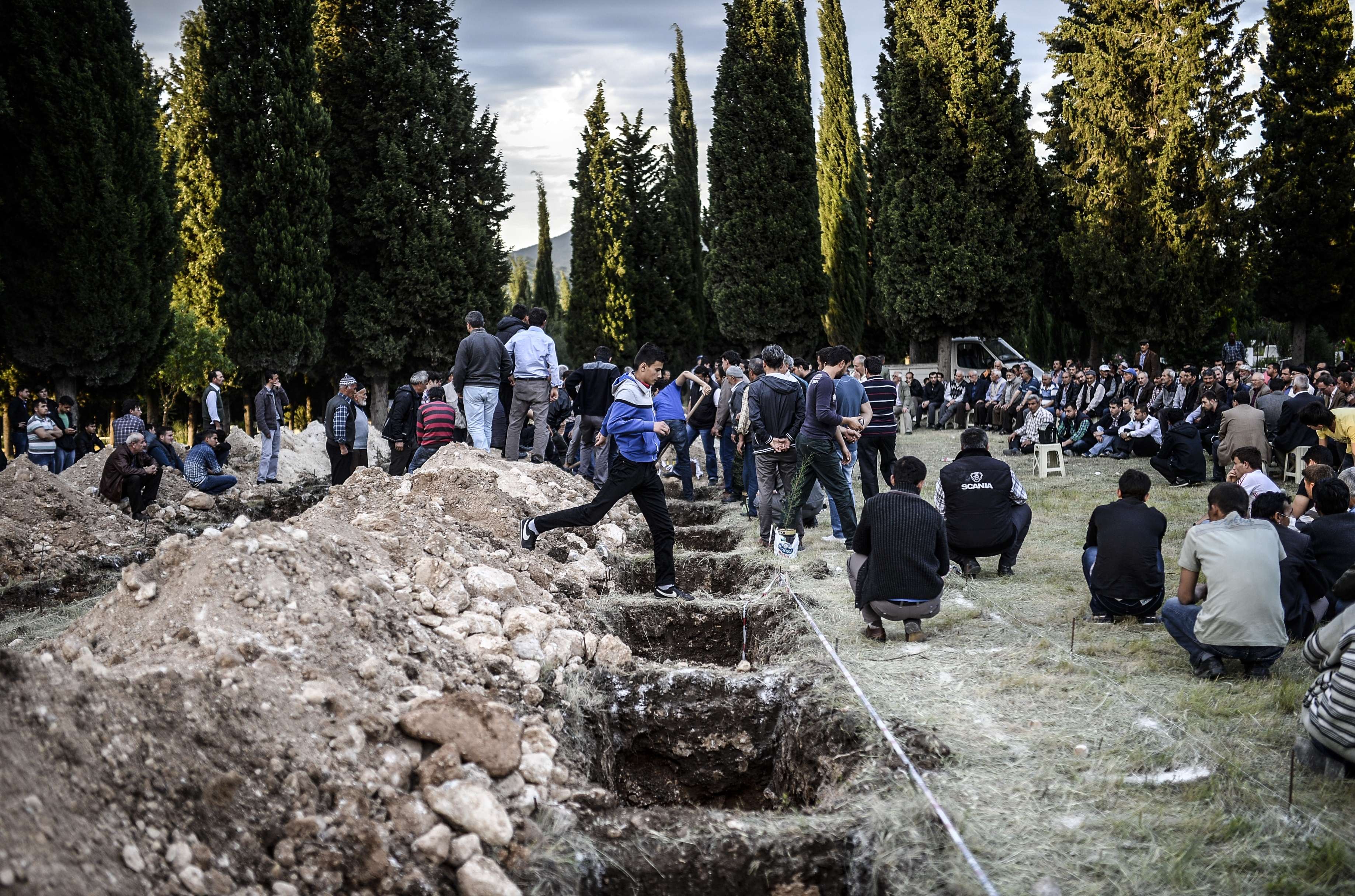 People sit near graves in a cemetary in Manisa on May 14, 2014, dug for the funeral of miners killed in a mine blast the day before in the western Turkish province of Manisa.