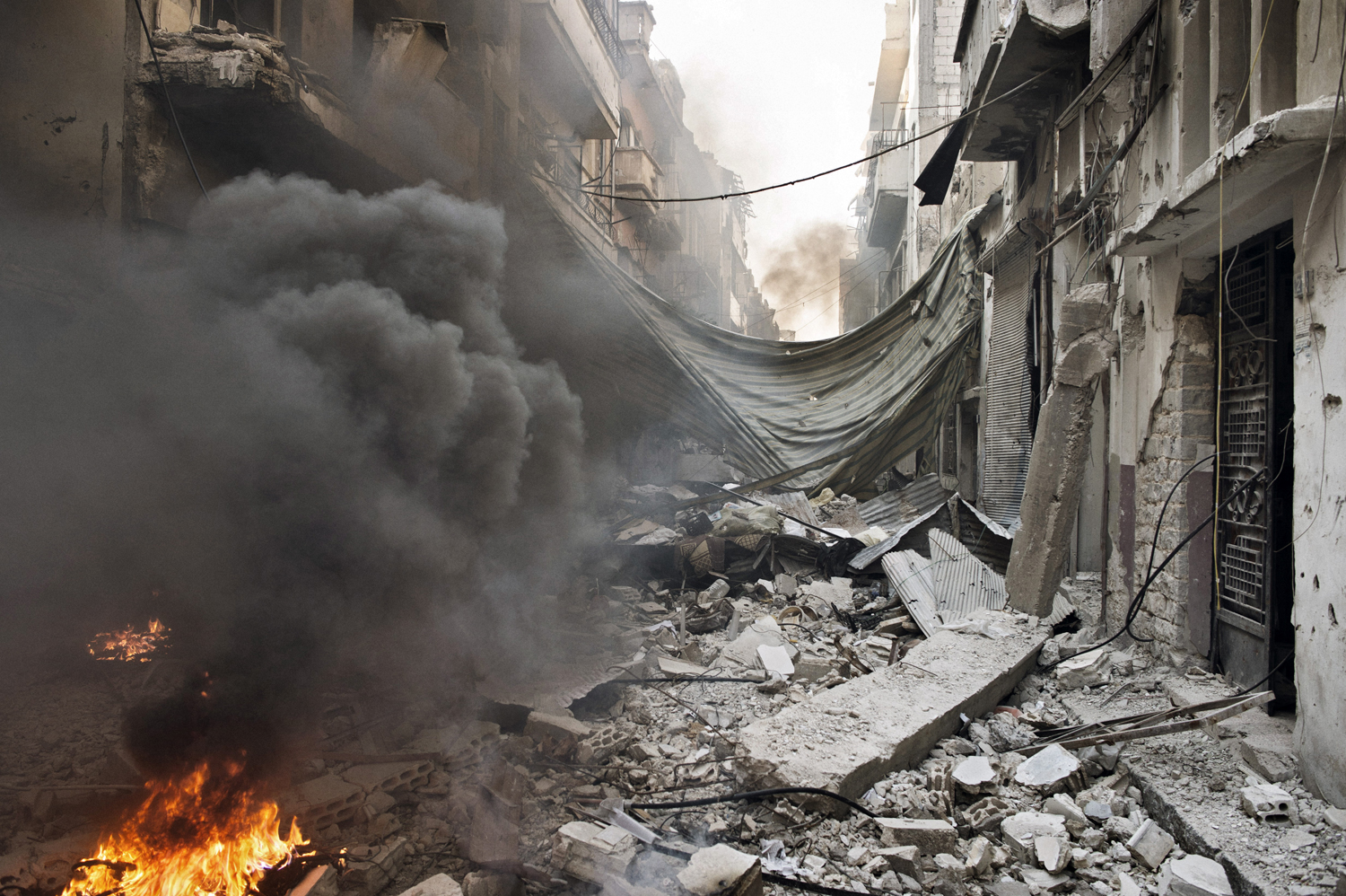 A street in the Qabaris neighborhood of Homs lies in ruins. Government soldiers use small fires to melt the plastic from cables and wires stripped from destroyed buildings. They say it is to prevent the wires from being used for improvised explosive devices, but the copper within can also be sold for cash. May 12, 2014.
