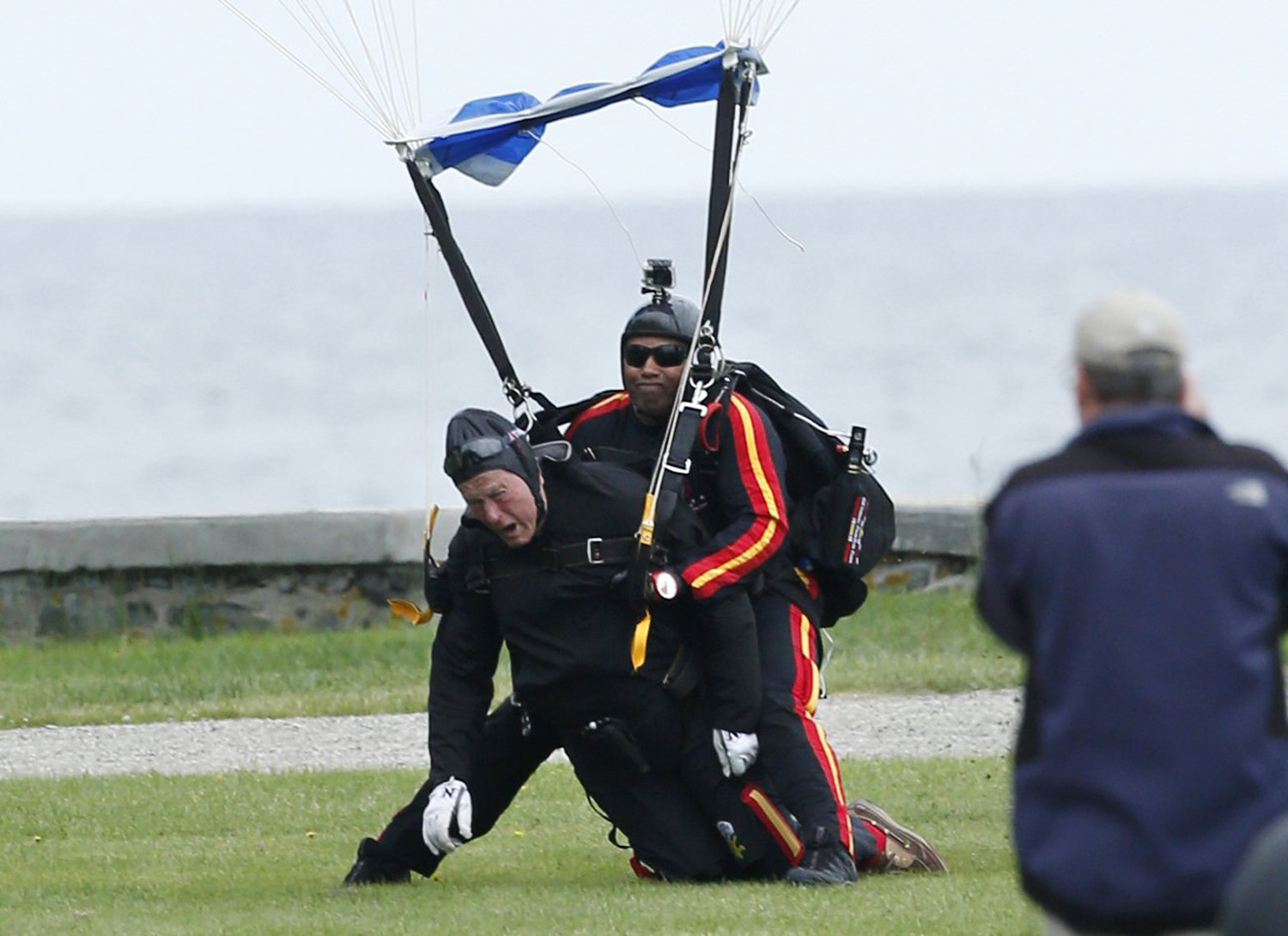 Former President George H.W. Bush, left, strapped to Sgt. 1st Class Mike Elliott, a retired member of the Army's Golden Knights parachute team, land on the lawn at St. Anne's Episcopal Church after making a tandem parachute jump to celebrate Bush's 90th birthday near his summer home in Kennebunkport, Maine, June 12, 2014.