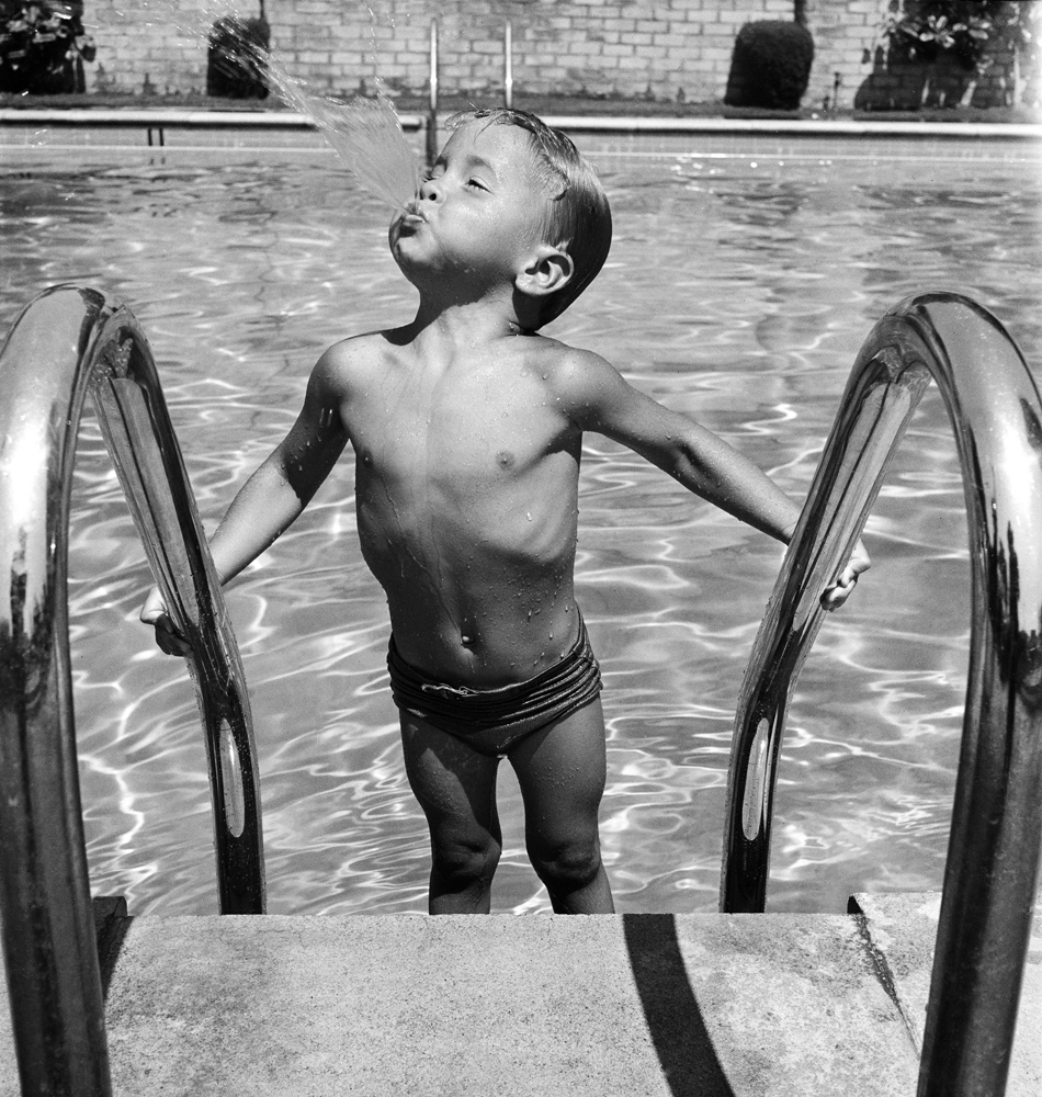 Duncan Richardson, 3-year-old swimming prodigy, playfully spews water while standing on a pool ladder, Los Angeles, 1946.