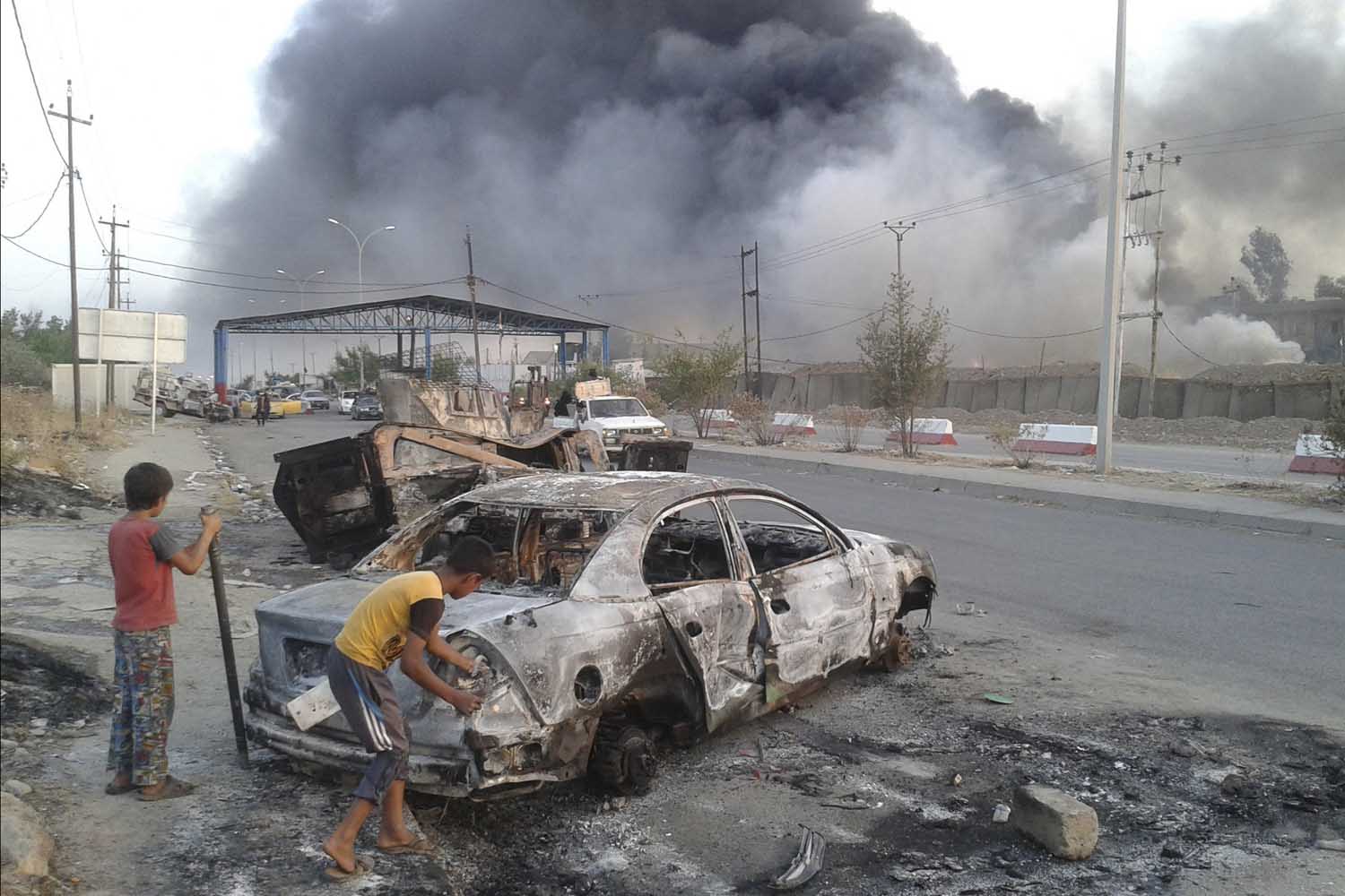 Civilian children stand next to a burnt vehicle during clashes between Iraqi security forces and al Qaeda-linked Islamic State in Iraq and the Levant (ISIL) in the northern Iraq city of Mosul