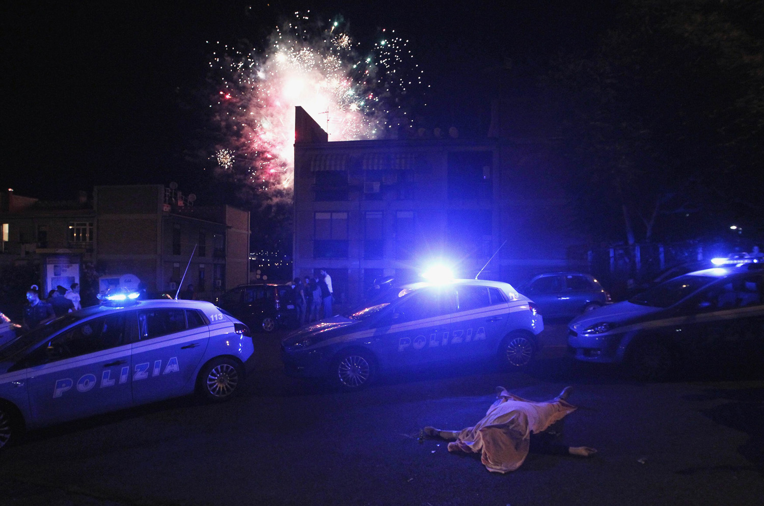 Police patrol area around man killed after shooting, as fireworks are set off at local party in background, in Naples