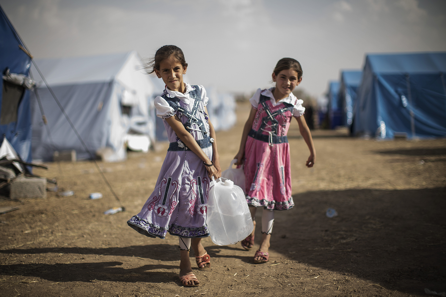 Iraqi children carry water to their tent at a temporary displacement camp set up next to a Kurdish checkpoint on June 13 in Kalak.
