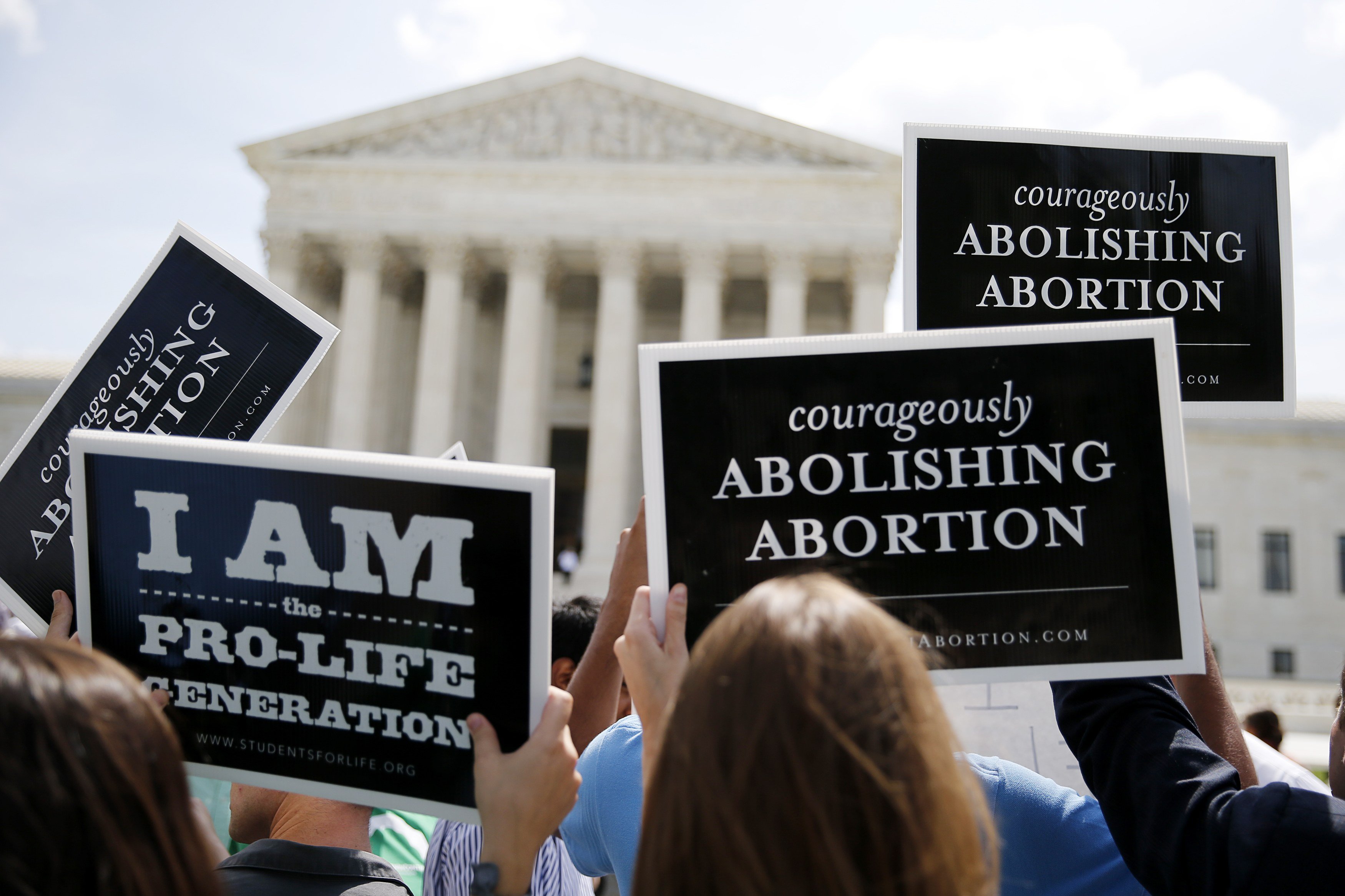 Anti-abortion protestors hold up signs as they celebrate U.S. Supreme Court ruling against protective buffer zones around abortion clinics, outside the Court in Washington