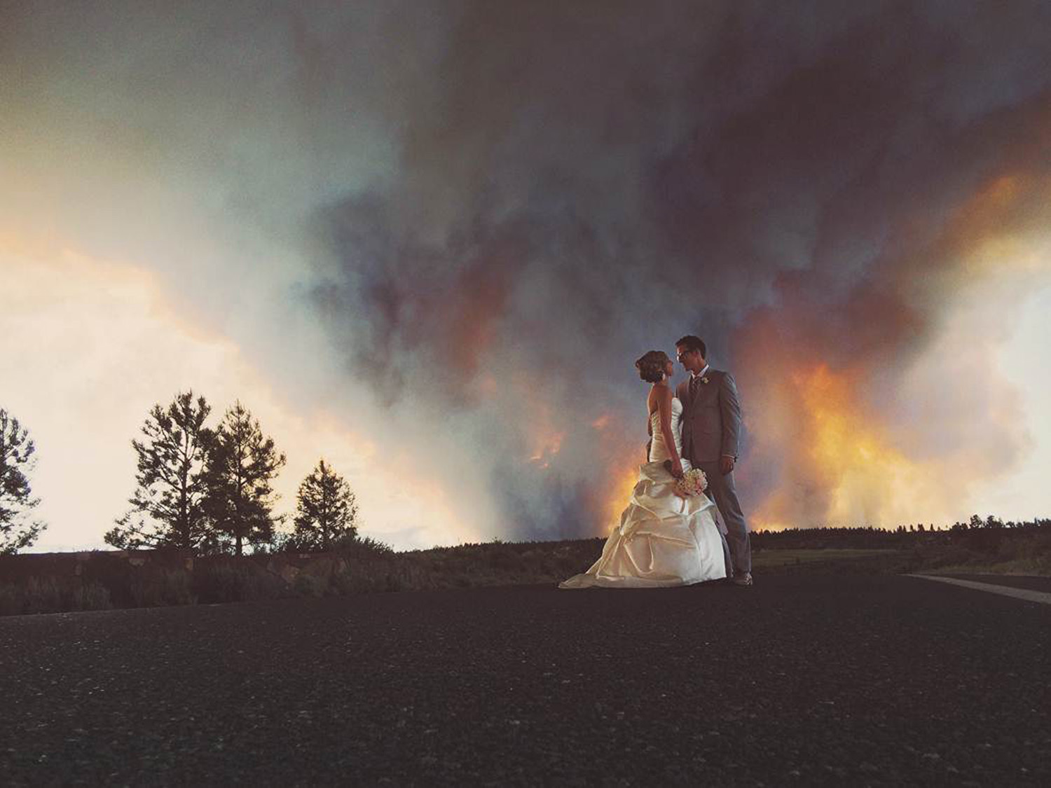 Newlyweds Michael Wolber and April Hartley pose for a picture as a wildfire burns in the background near Bend, Ore., June 7, 2014.