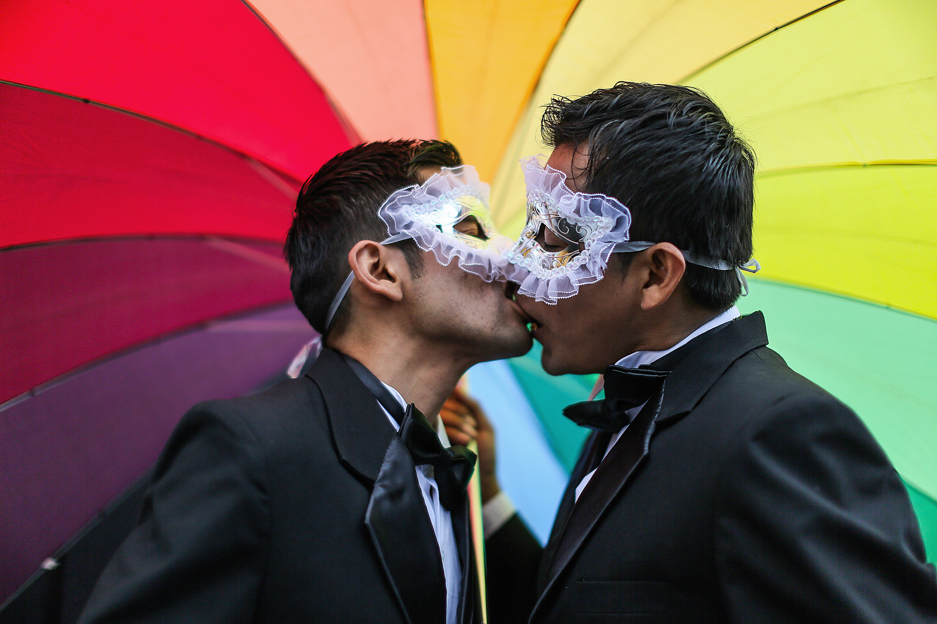 Men kiss under a rainbow umbrella during a gay pride parade in Lima, Peru, Saturday, June 28, 2014.