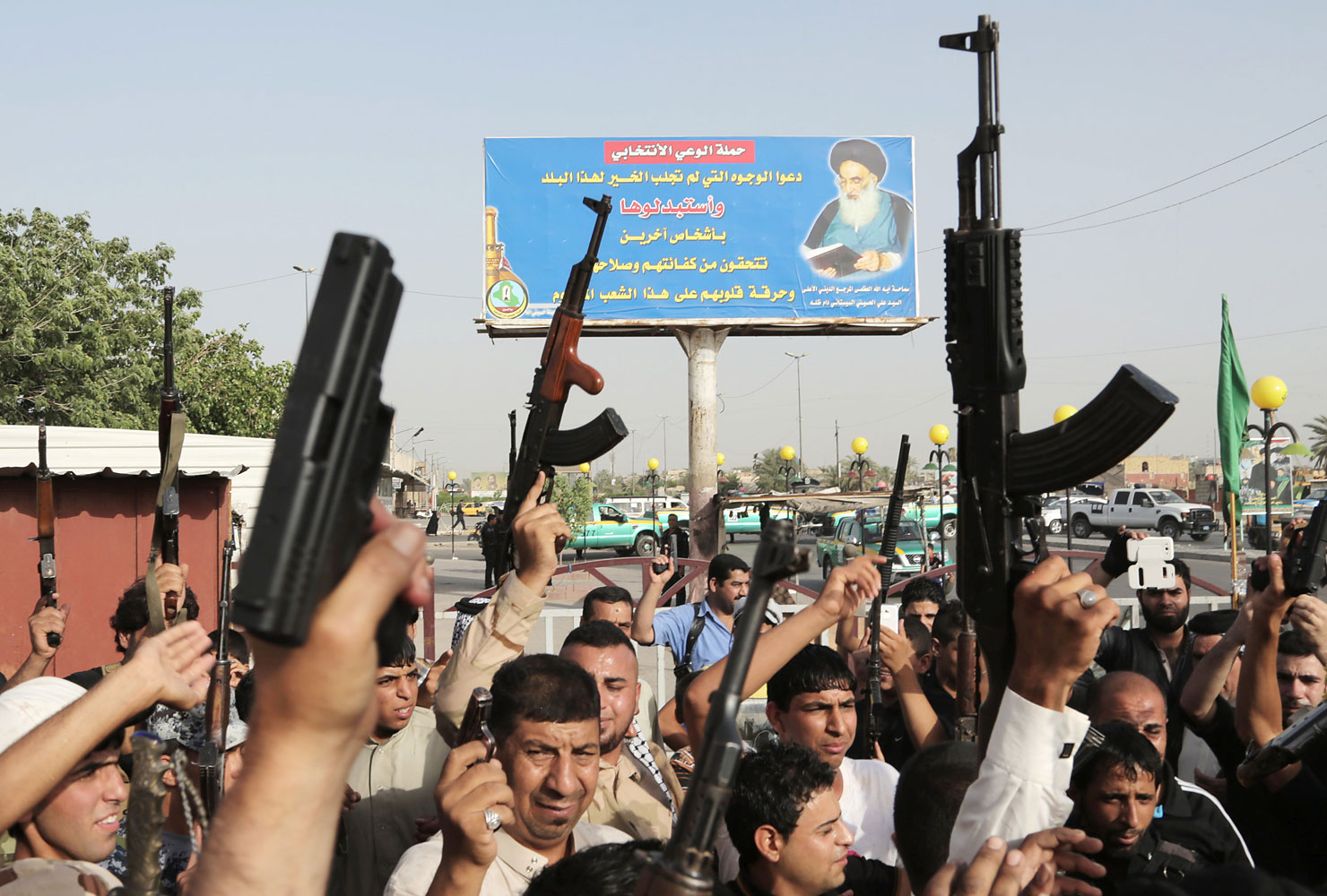 Iraqi Shiite tribal fighters raise their weapons and chant slogans against the al-Qaida-inspired Islamic State of Iraq and the Levant below a portrait of Ayatollah Ali al-Sistani, in Baghdad's Sadr City, Iraq, June 18, 2014. On Friday, Grand Ayatollah Ali al-Sistani, Iraq's top Shiite cleric, called for a new effective government in Iraq. (Khalid Mohammed—AP)