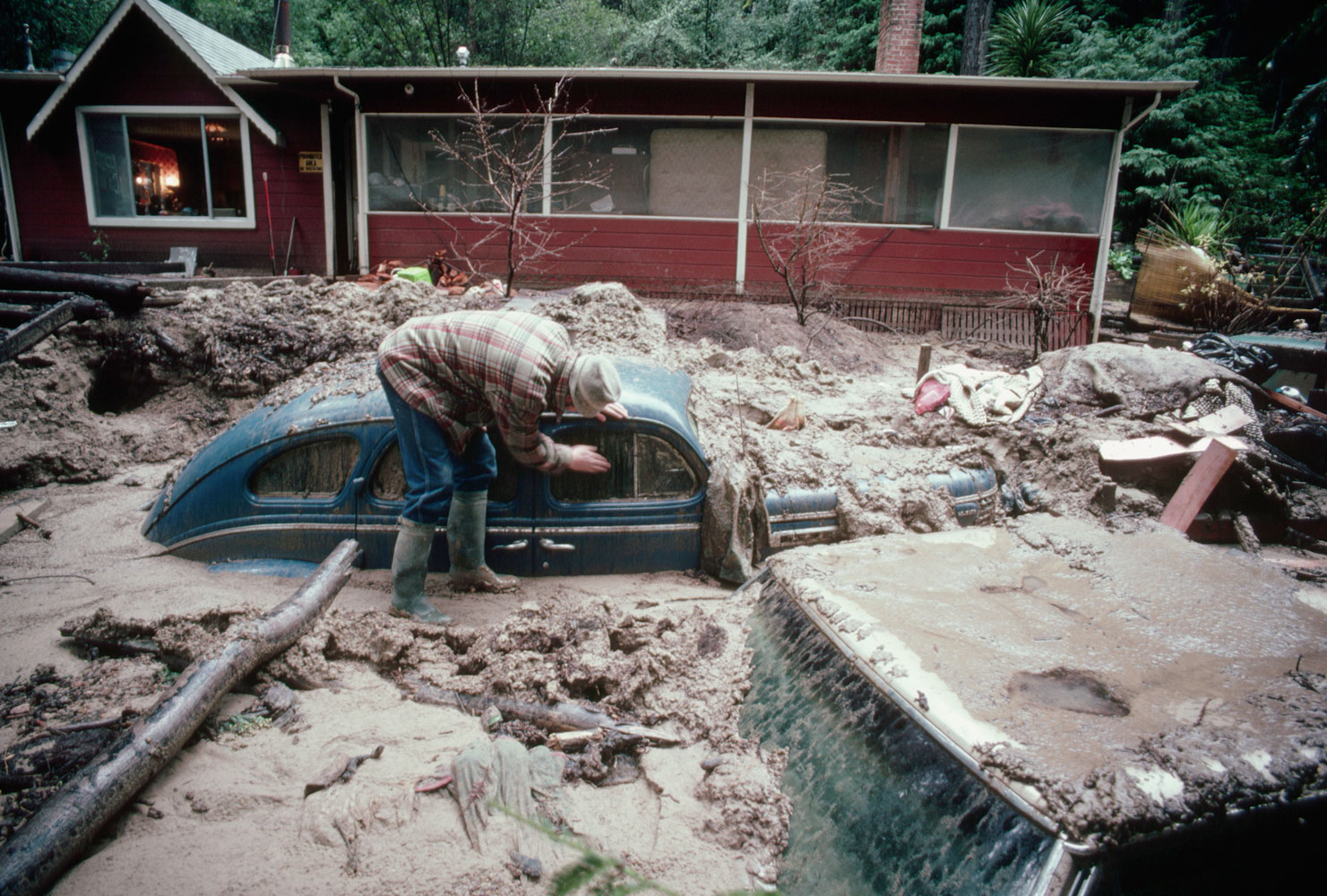 A man attempts to excavate an old car buried by a mudslide, most likely triggered by El Nino-induced rains on January 1, 1981.