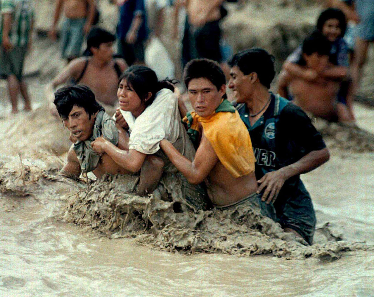 Three men help a woman trying to cross the overflowing Nepena River in Chimbote, Peru on Feb. 26, 1998. The meteorological phenomenon El Nino created ravaging weather conditions that killed many throughout Peru.