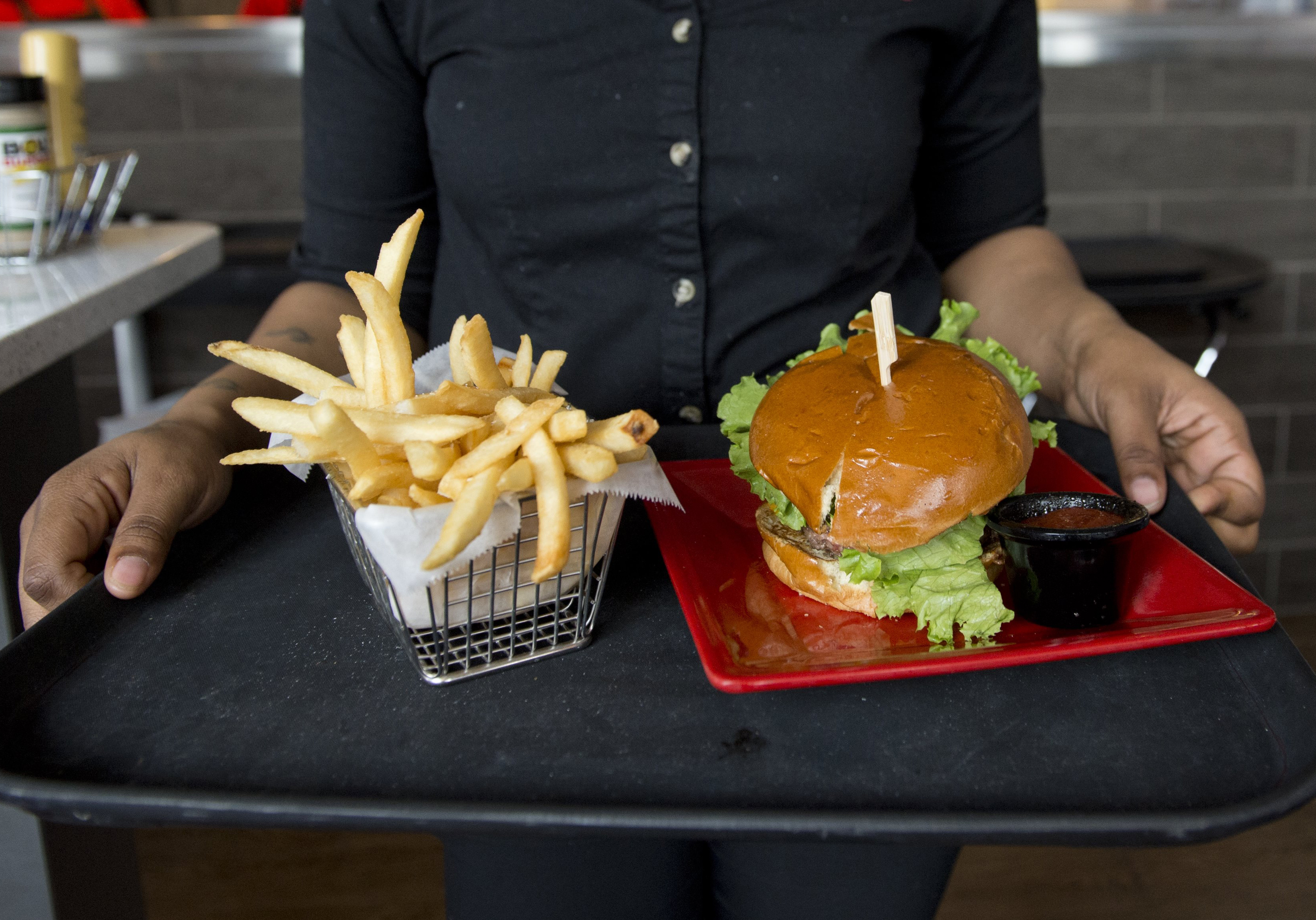 A server carries a tray with a hamburger and french fries at Bolt Burgers in Washington, DC on February 25, 2014. 