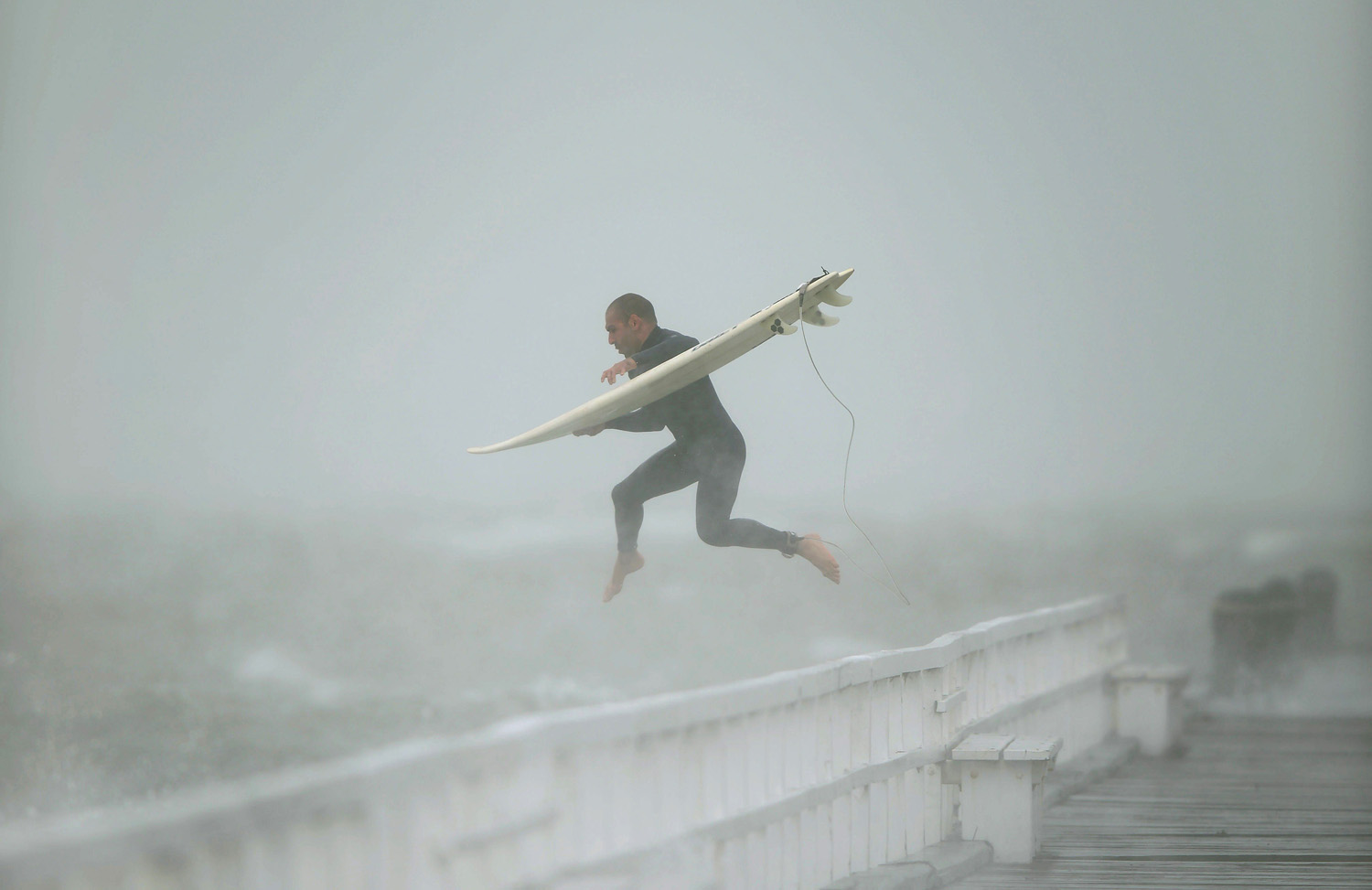 A surfer jumps off the pier into Port Phillip Bay to take advantage of the waves as a storm lashes the Melbourne area on June 24, 2014.