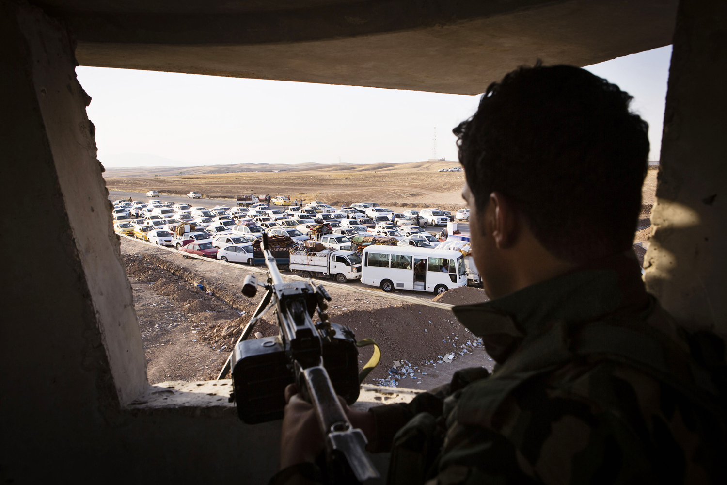 An Iraqi security forces member with his weapon takes position as people, who fled from the violence in Mosul, arrive in their vehicles at a camp for internally displaced people on the outskirts of Erbil in Iraq's Kurdistan region June 14.