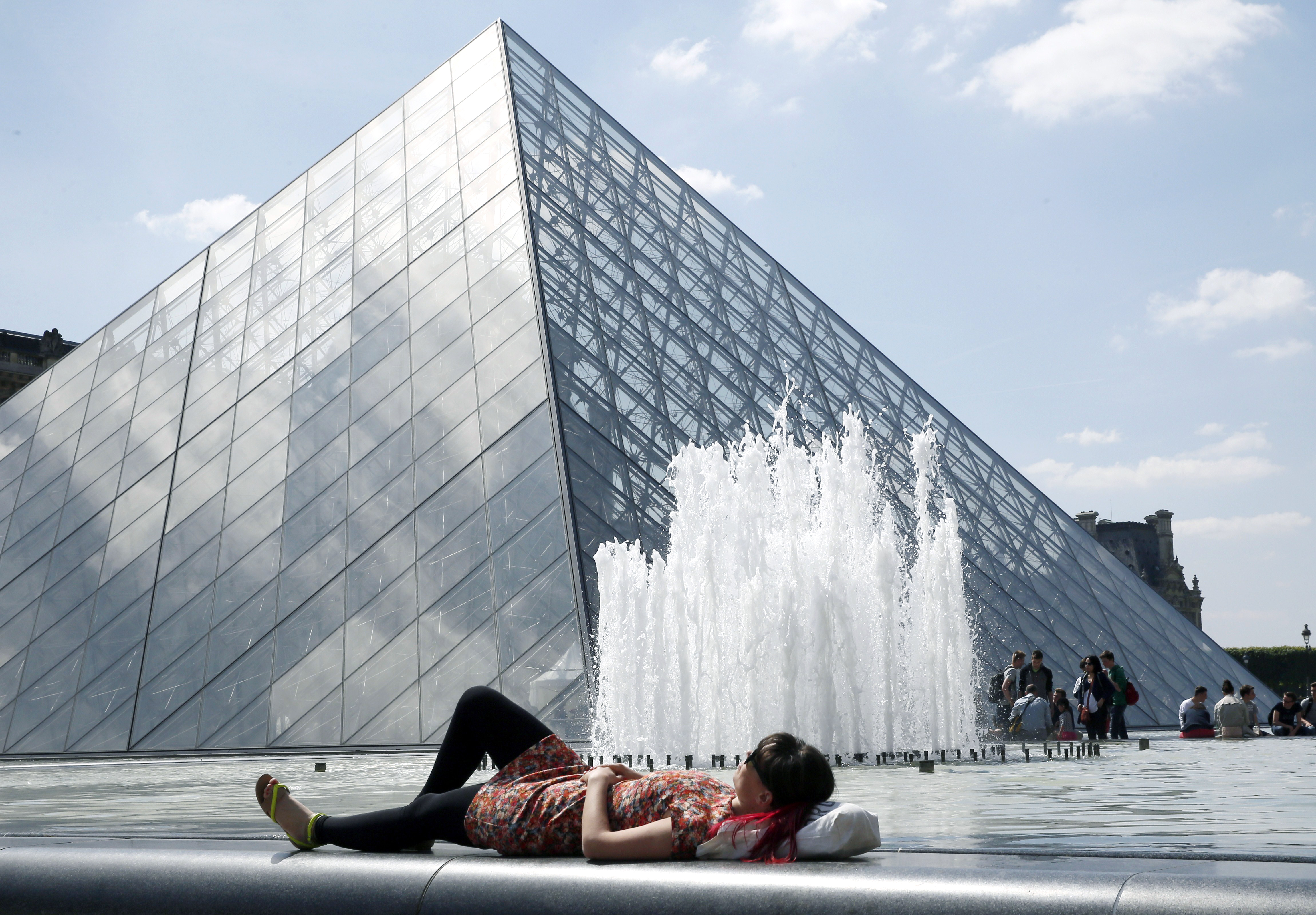 A woman enjoys the sunny weather near the Louvre Museum pyramid in Paris on May 16, 2014. (Patrick Kovarik—AFP/Getty Images)