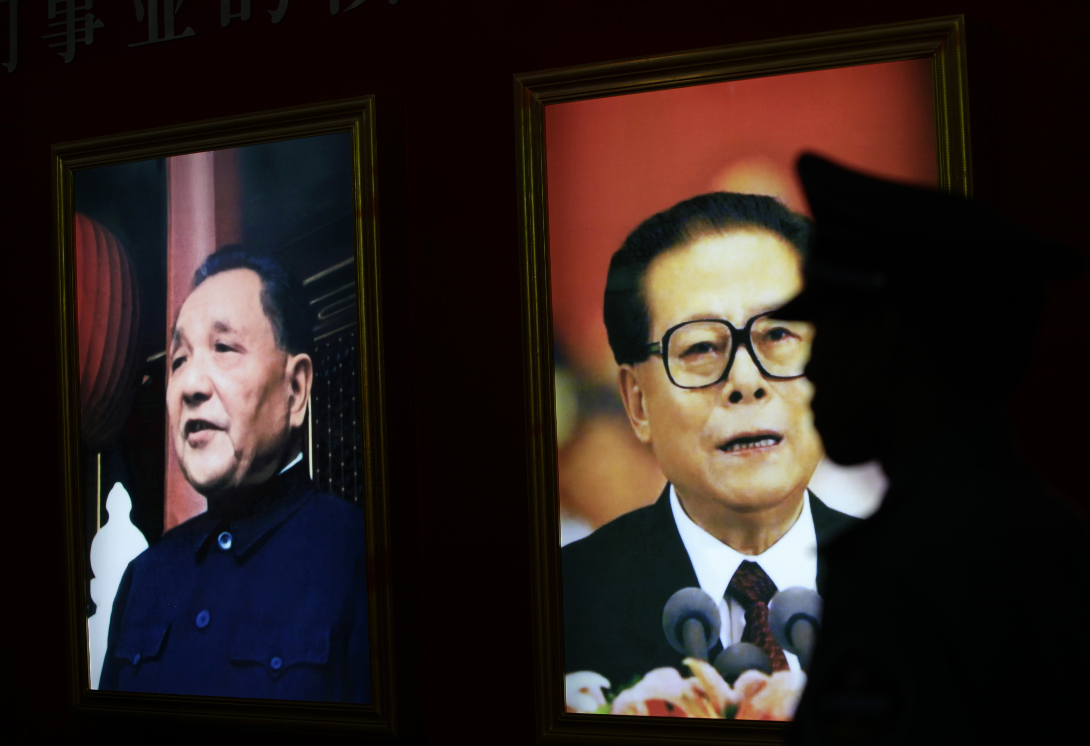 A security guard stands next to pictures of China's former President Jiang Zemin and late paramount leader Deng Xiaoping at an exhibition in Beijing