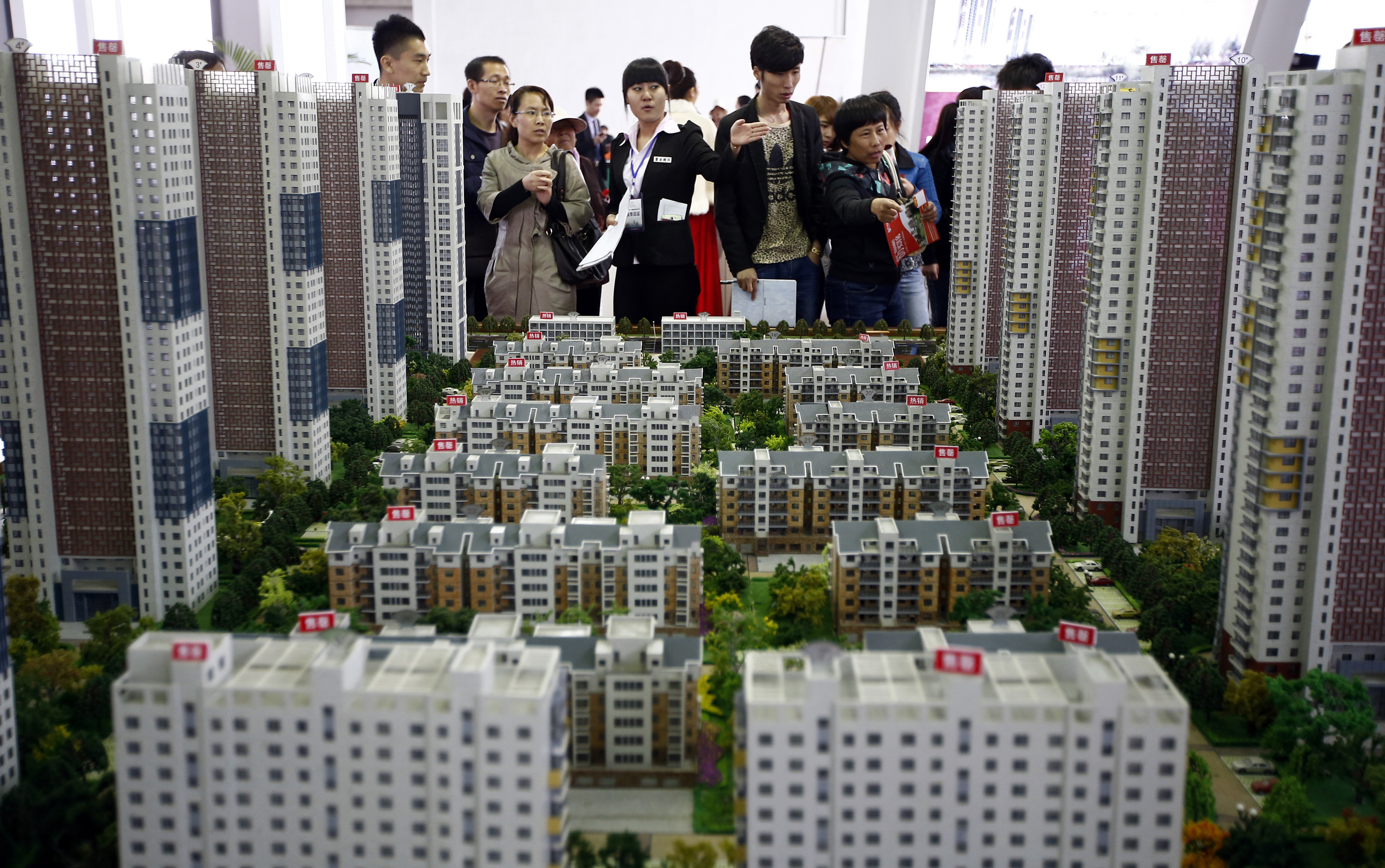 A sales assistant talks to visitors in front of models of apartments at a real estate exhibition in Shenyang